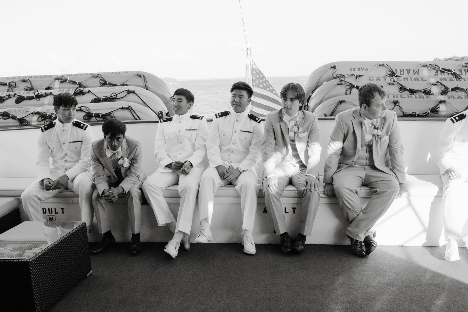 Groomsmen in white uniforms sit casually in a row during wedding festivities.