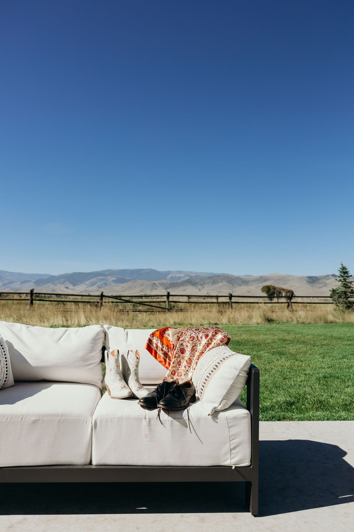 An outdoor white couch with orange throw pillows overlooking mountain views.