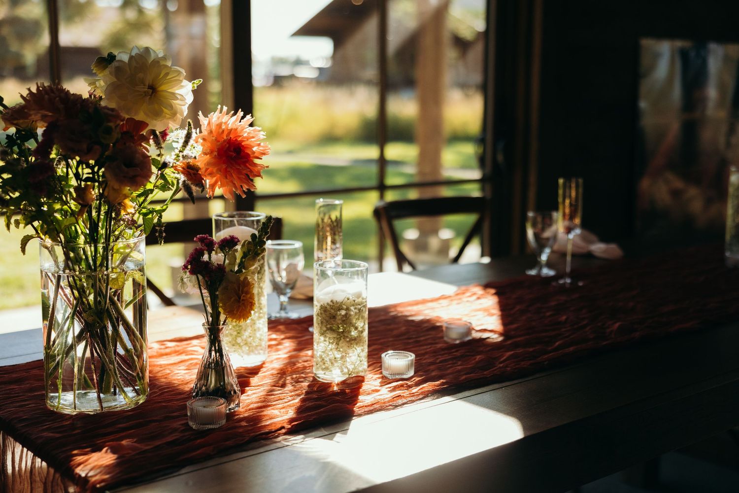 Sunlit wedding reception table with floral centerpieces and glassware.