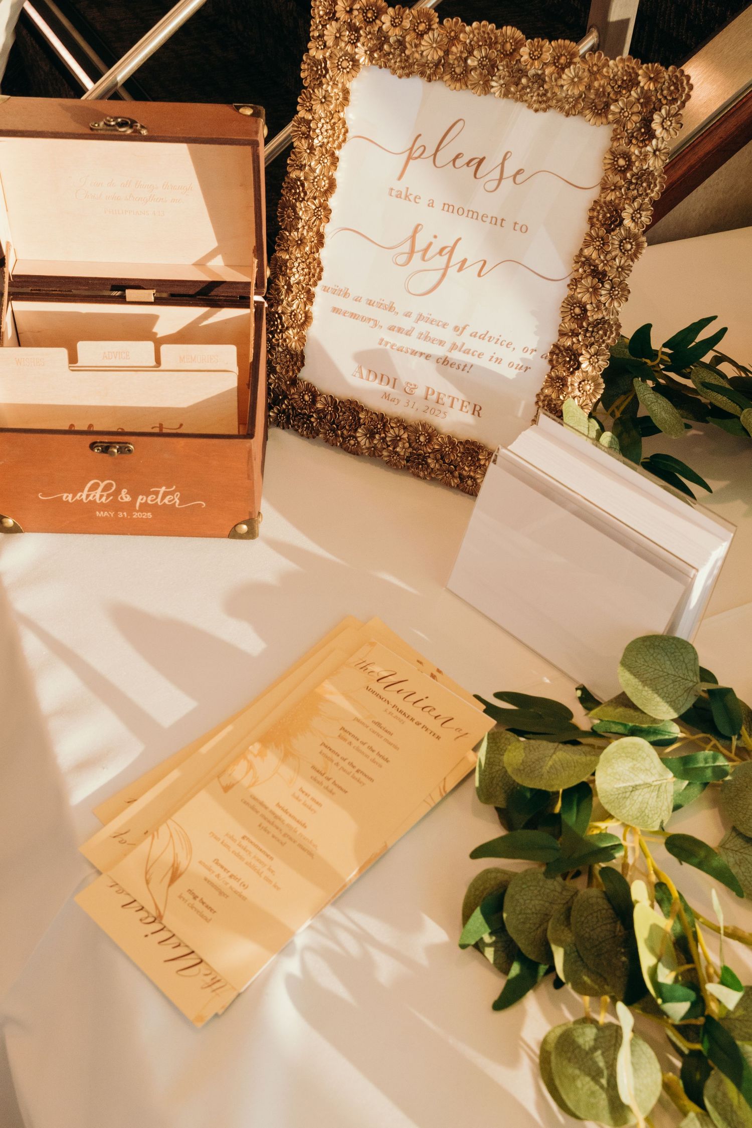 Wedding invitation suite in blush and gold tones with ornate frames and greenery accents.