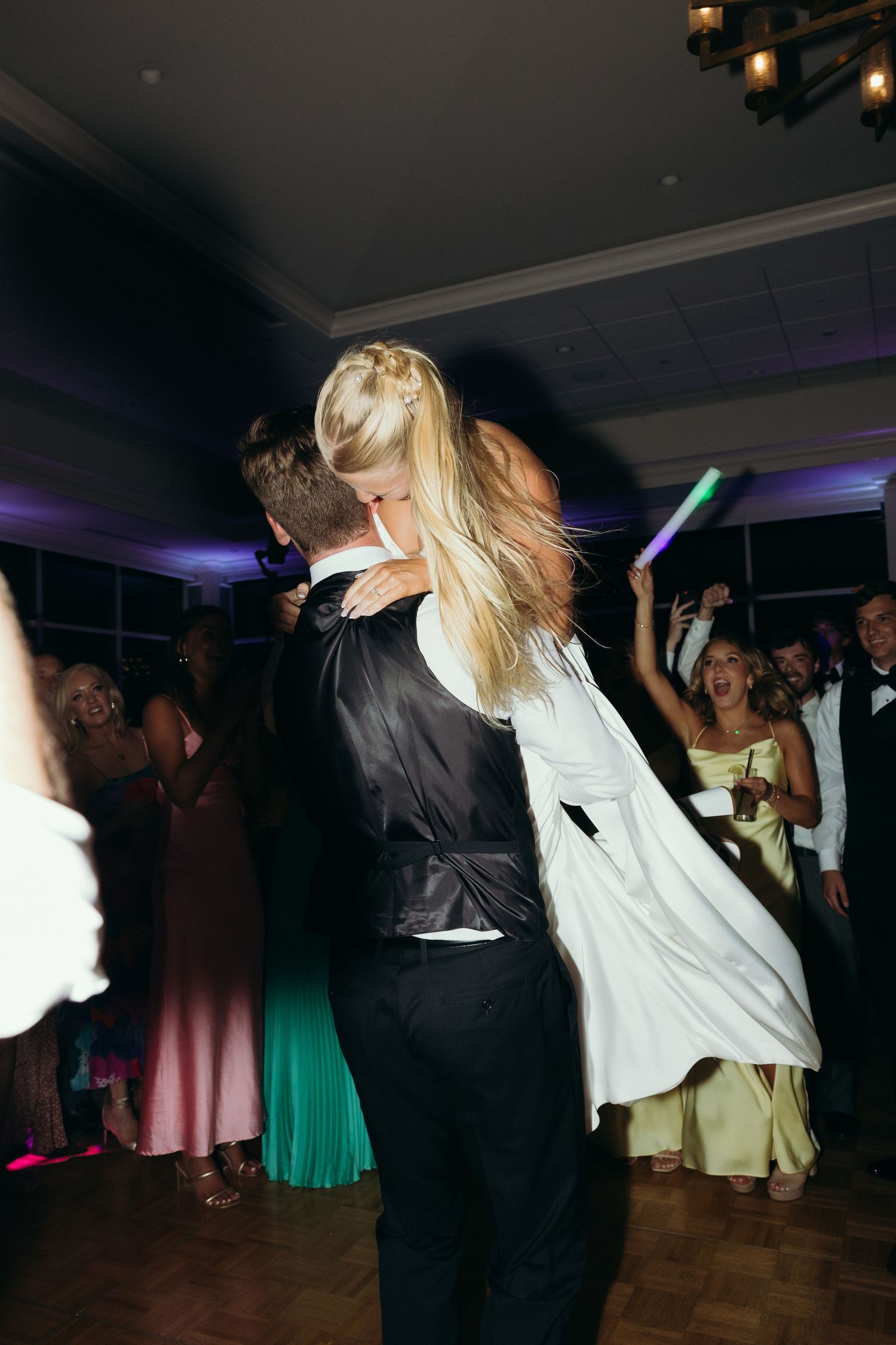 Wedding guests dancing and celebrating on a dark dance floor with atmospheric lighting.