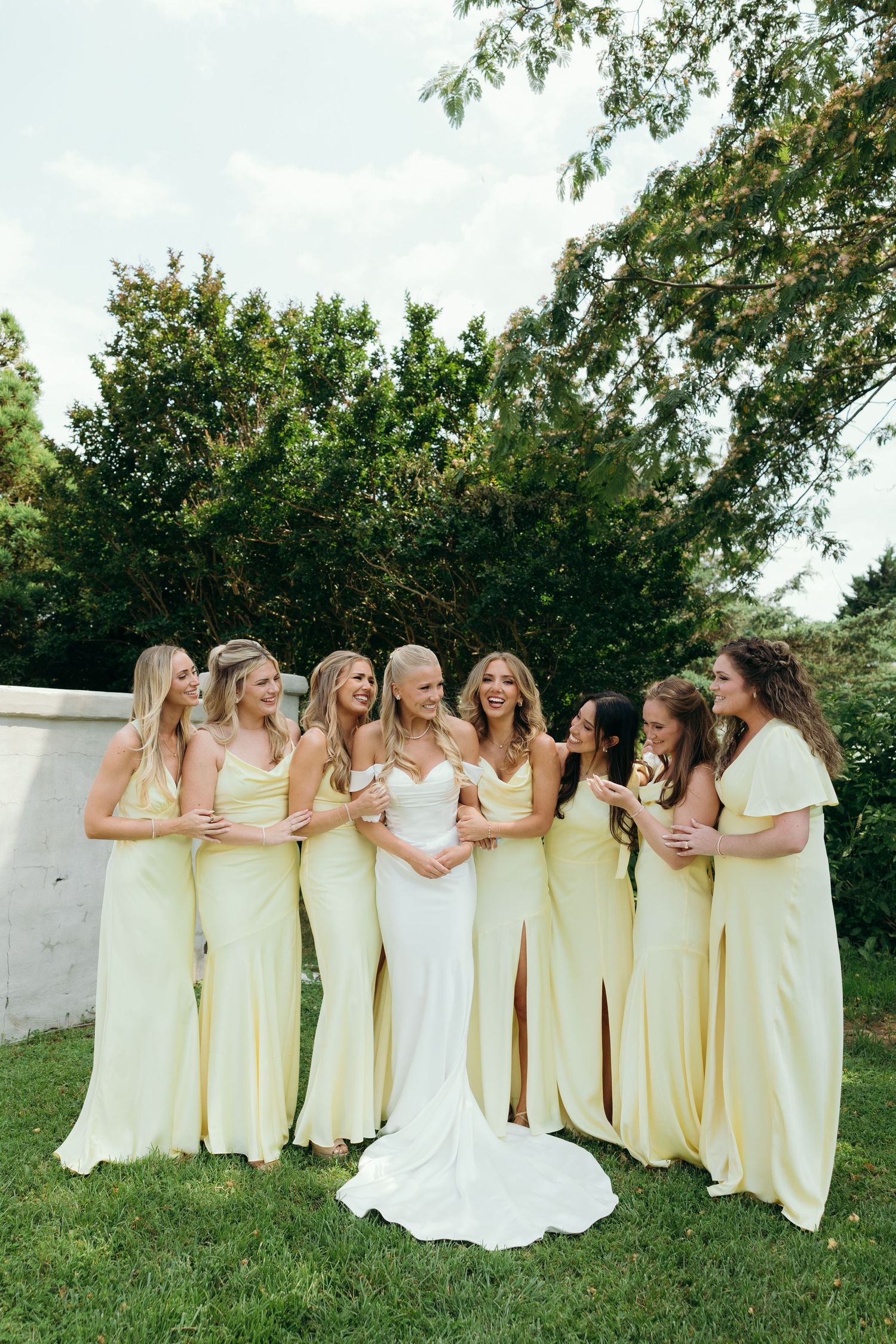 Wedding party in yellow bridesmaid dresses and white bridal gown posing on grass.