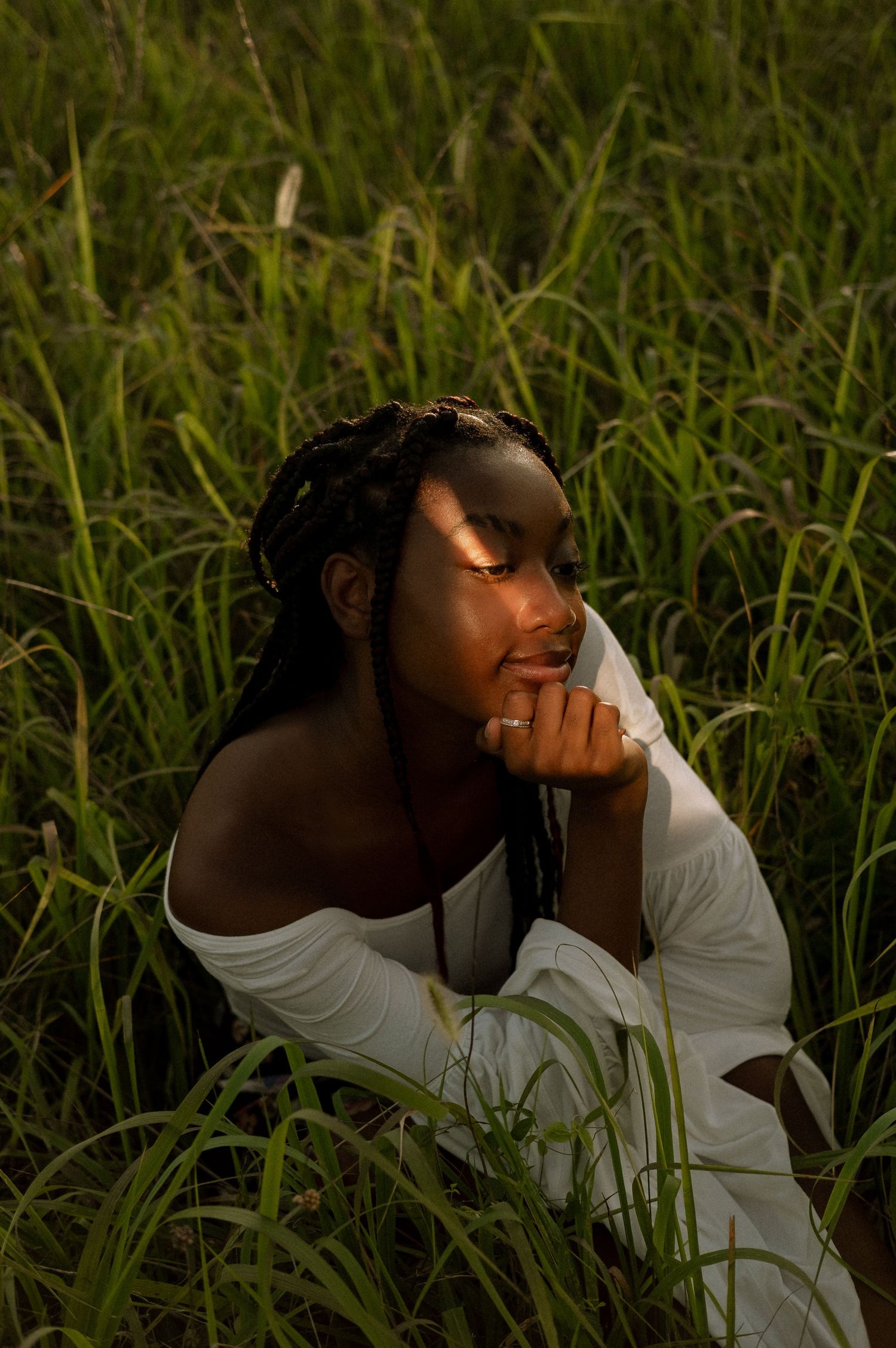 Photo of a senior girl sitting in a field at golden hour with a strip of light across her face