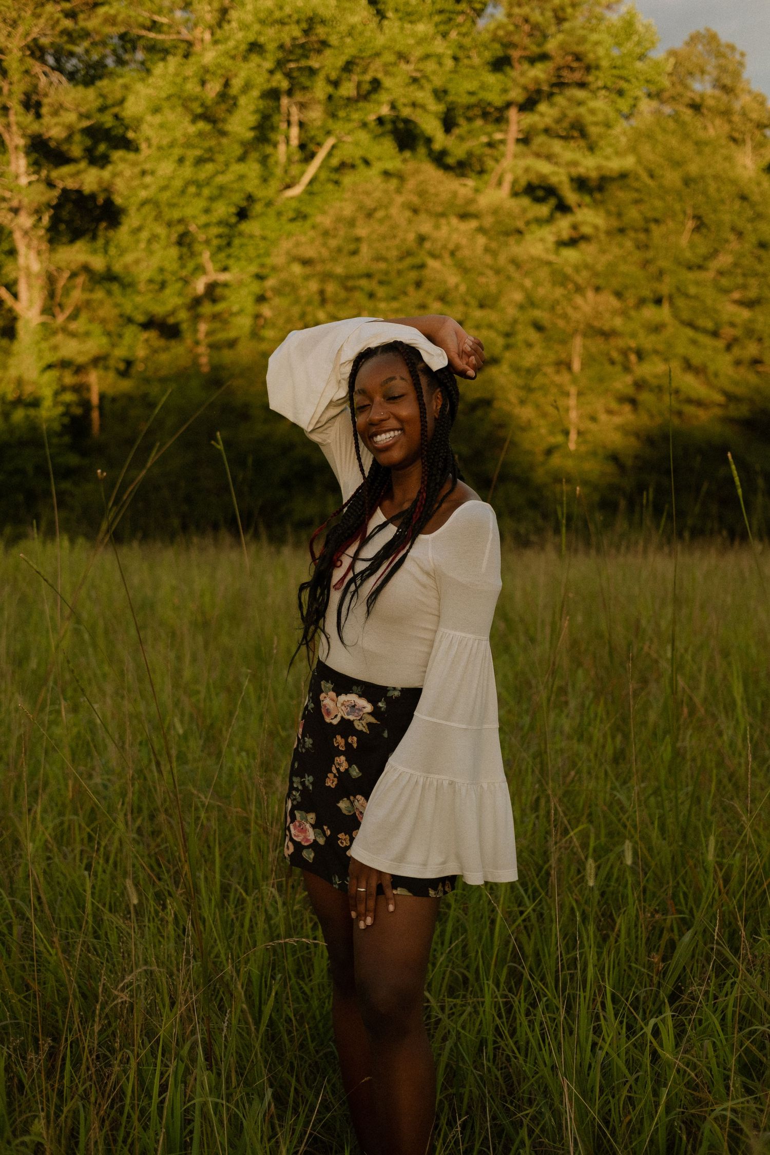 Photo of a senior girl standing in a field at golden hour with her arm above her head