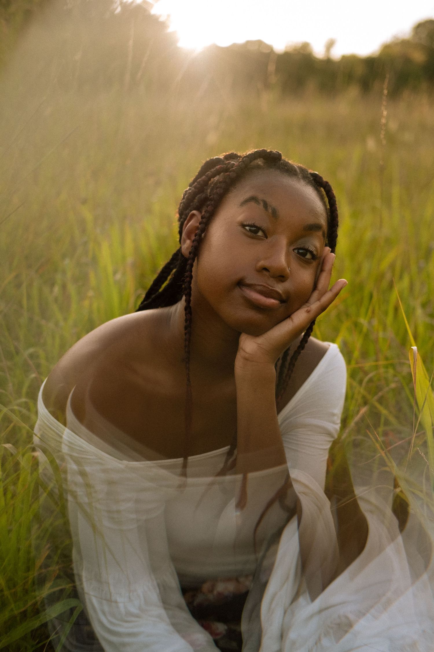 Photo of a senior girl sitting in a field at golden hour with prism effects