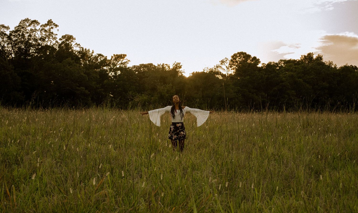 Photo of a senior girl standing in a field at golden hour with both arms up