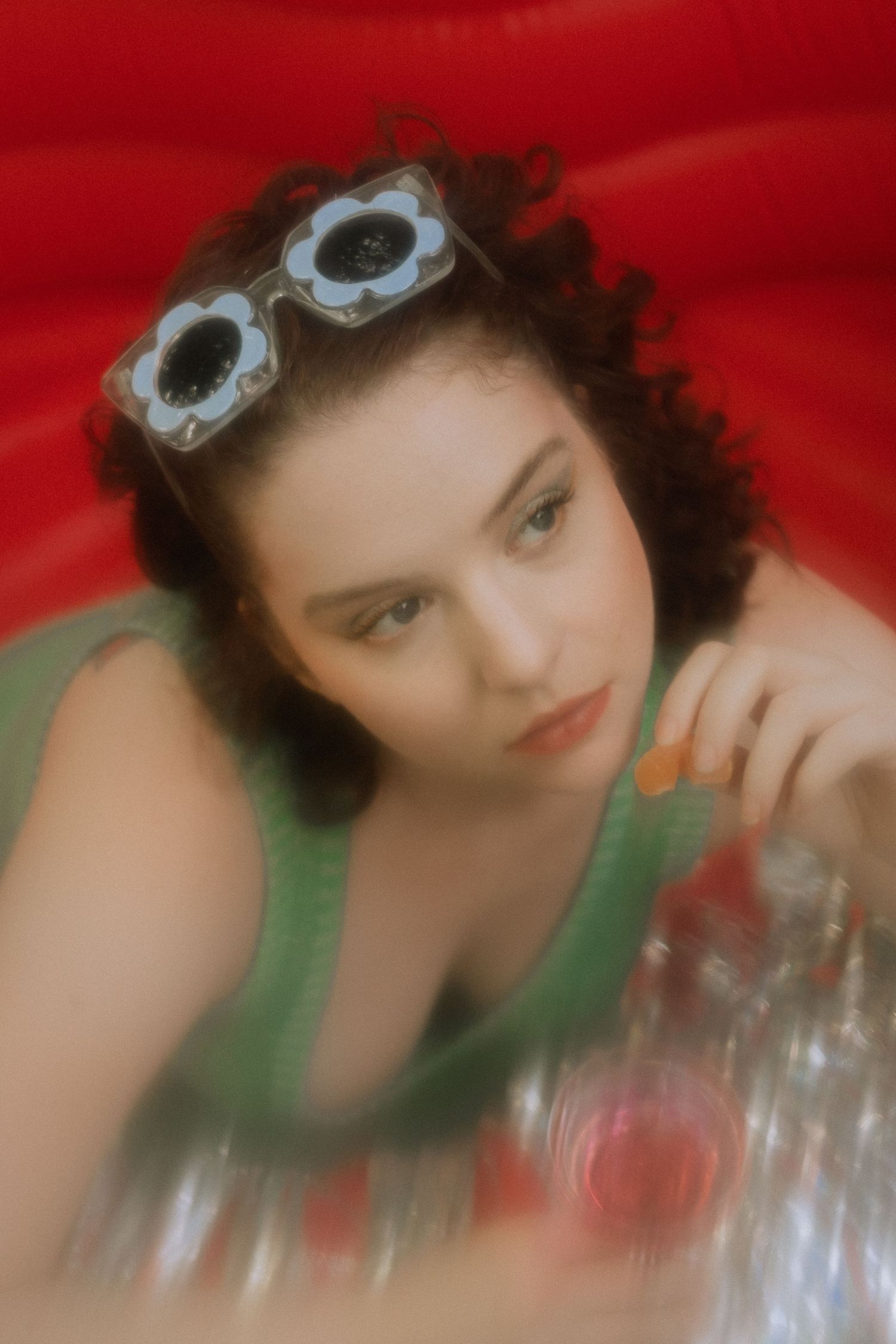 Girl with blue flower sunglasses in red pool with drink in hand