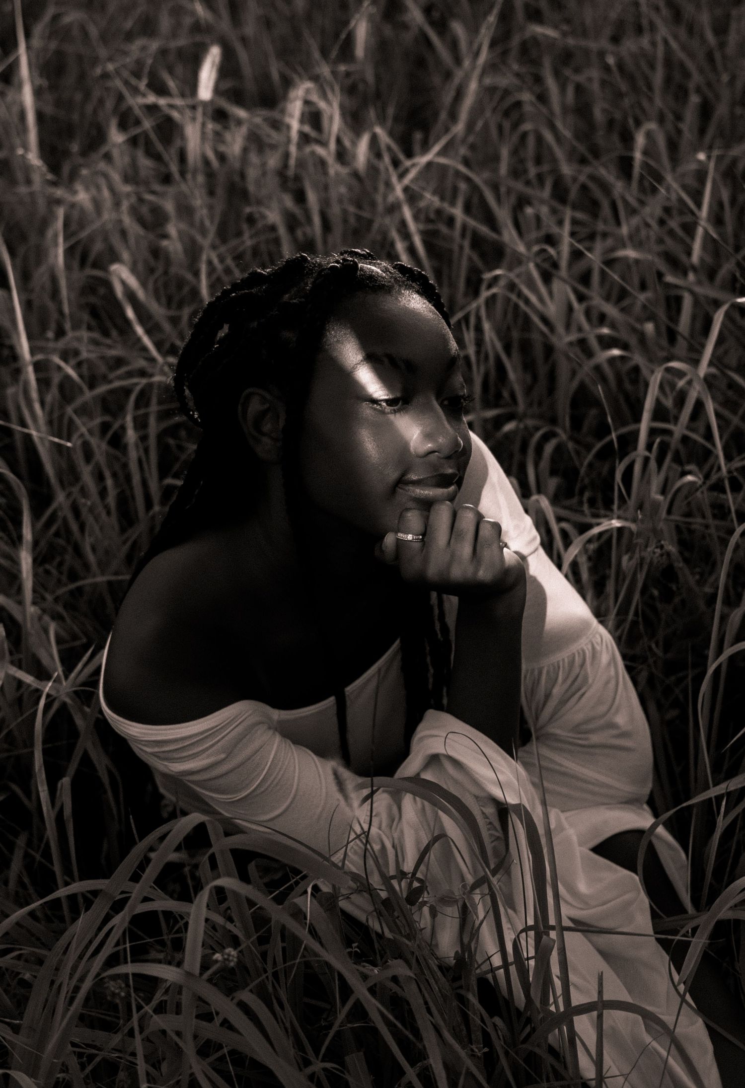 Black and white photo of a senior girl sitting in a field at golden hour with a strip of light across her face