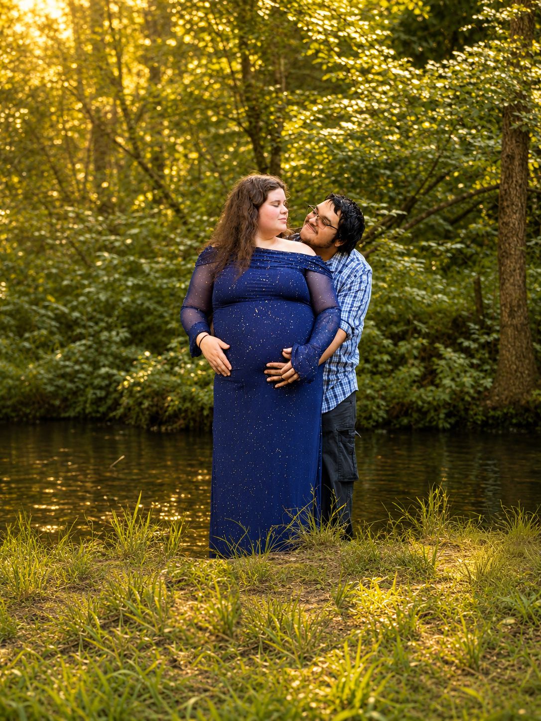 A pregnant woman posing in a river with her lover standing behind her in support of them getting ready for their babies arrival.