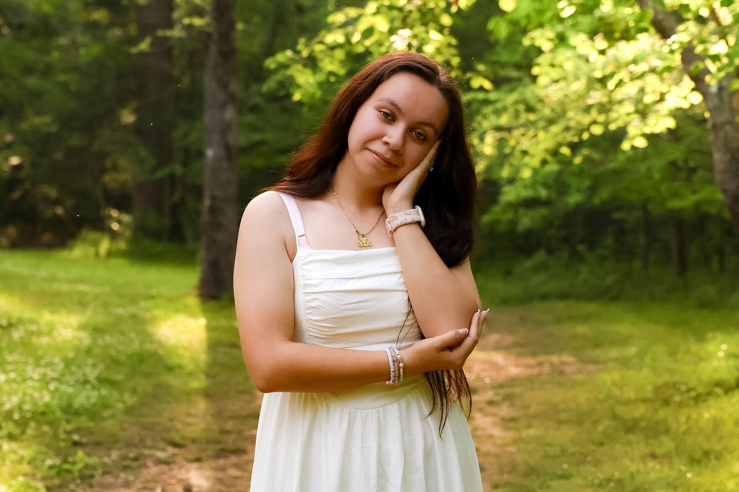 A young woman posing with her hand on her head and the other holding her arm up posing for her senior session.