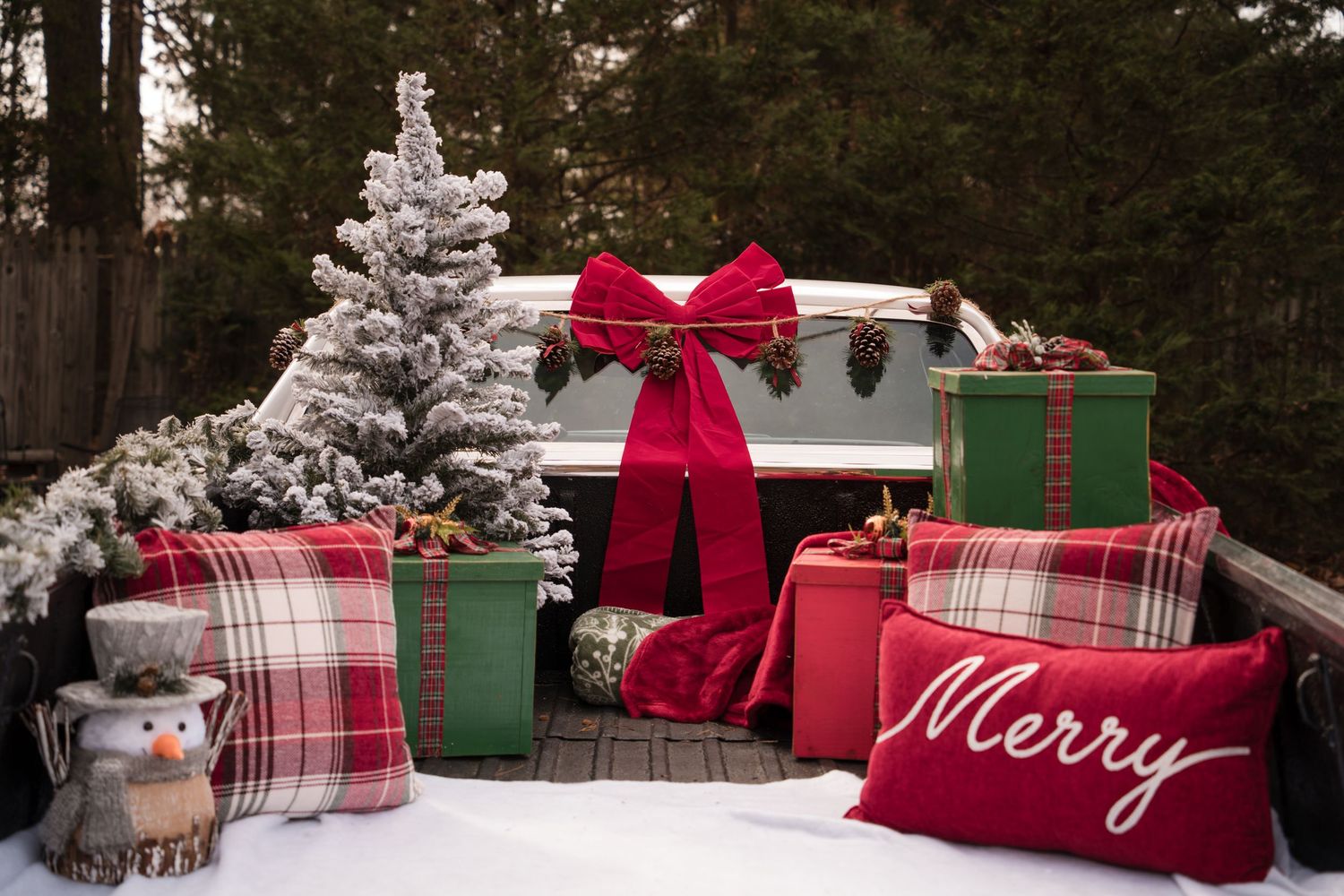 Christmas presents wrapped in red and plaid paper with silver decorations arranged on a rustic wooden deck outdoors.
