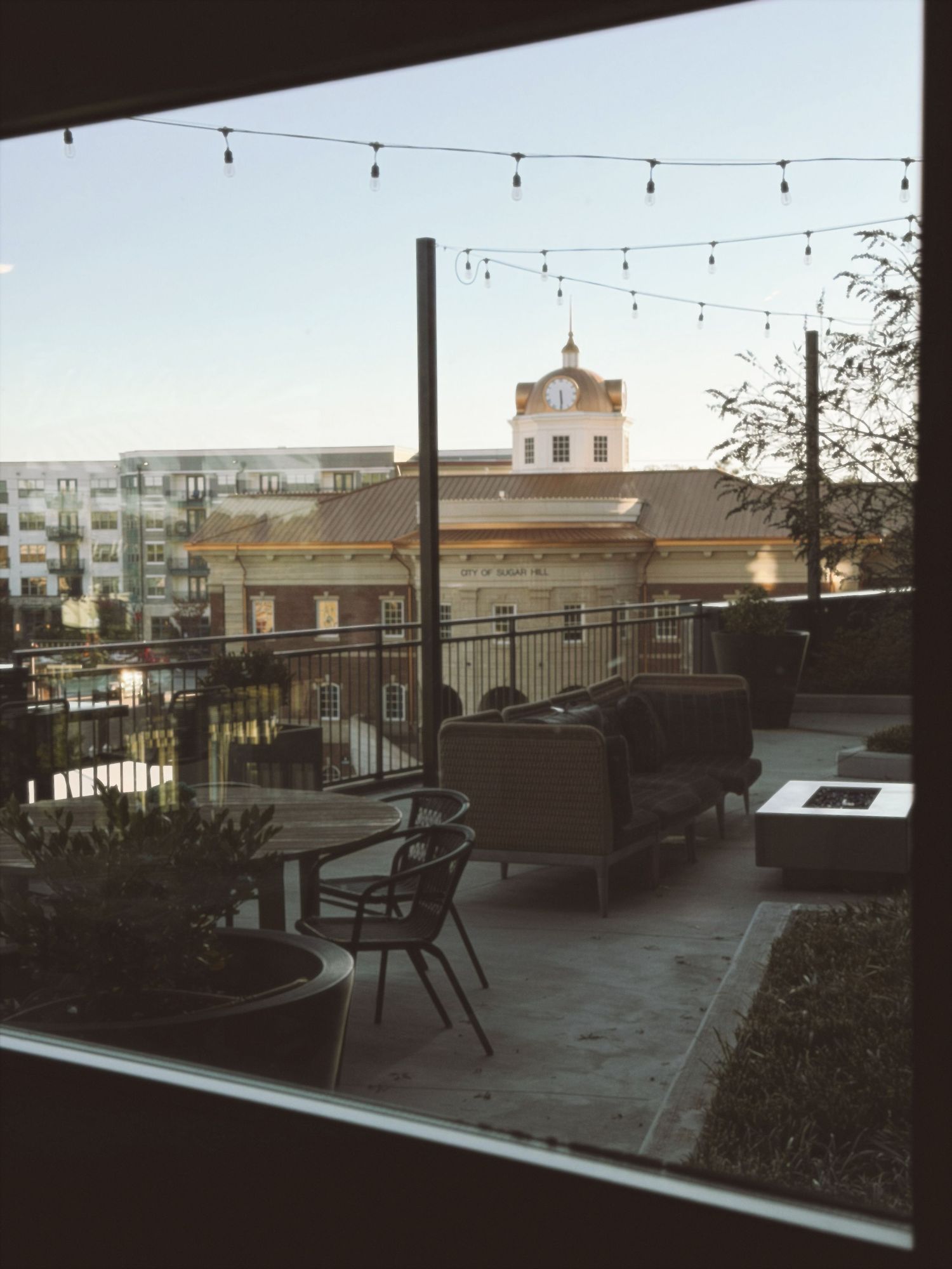 A modern outdoor patio seating area with chairs and string lights at dusk overlooking residential buildings.