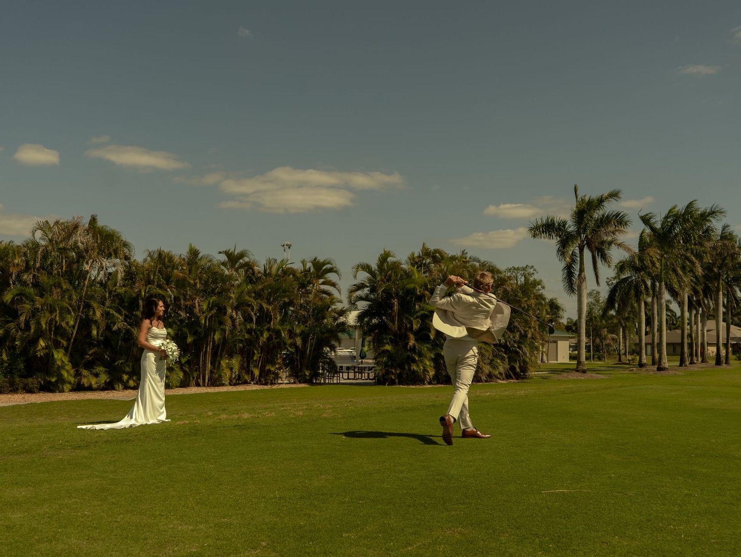 Bride and groom celebrate on lush green lawn surrounded by tropical palm trees under a clear blue sky.
