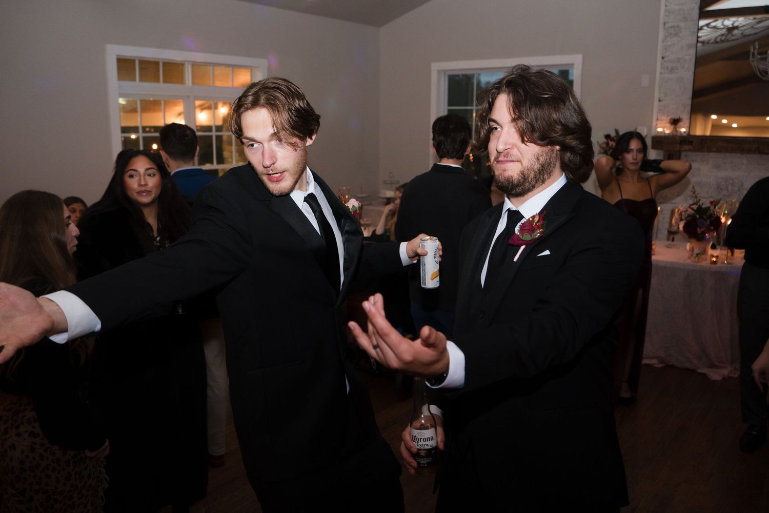 Wedding guests mingle and dance together during an evening reception celebration at an indoor venue.