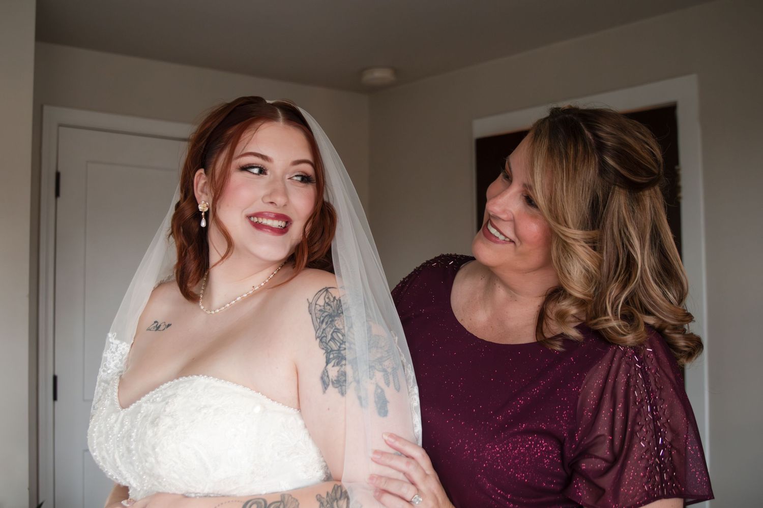 Two people share a joyful moment together, one wearing a white wedding dress and the other in a burgundy top.