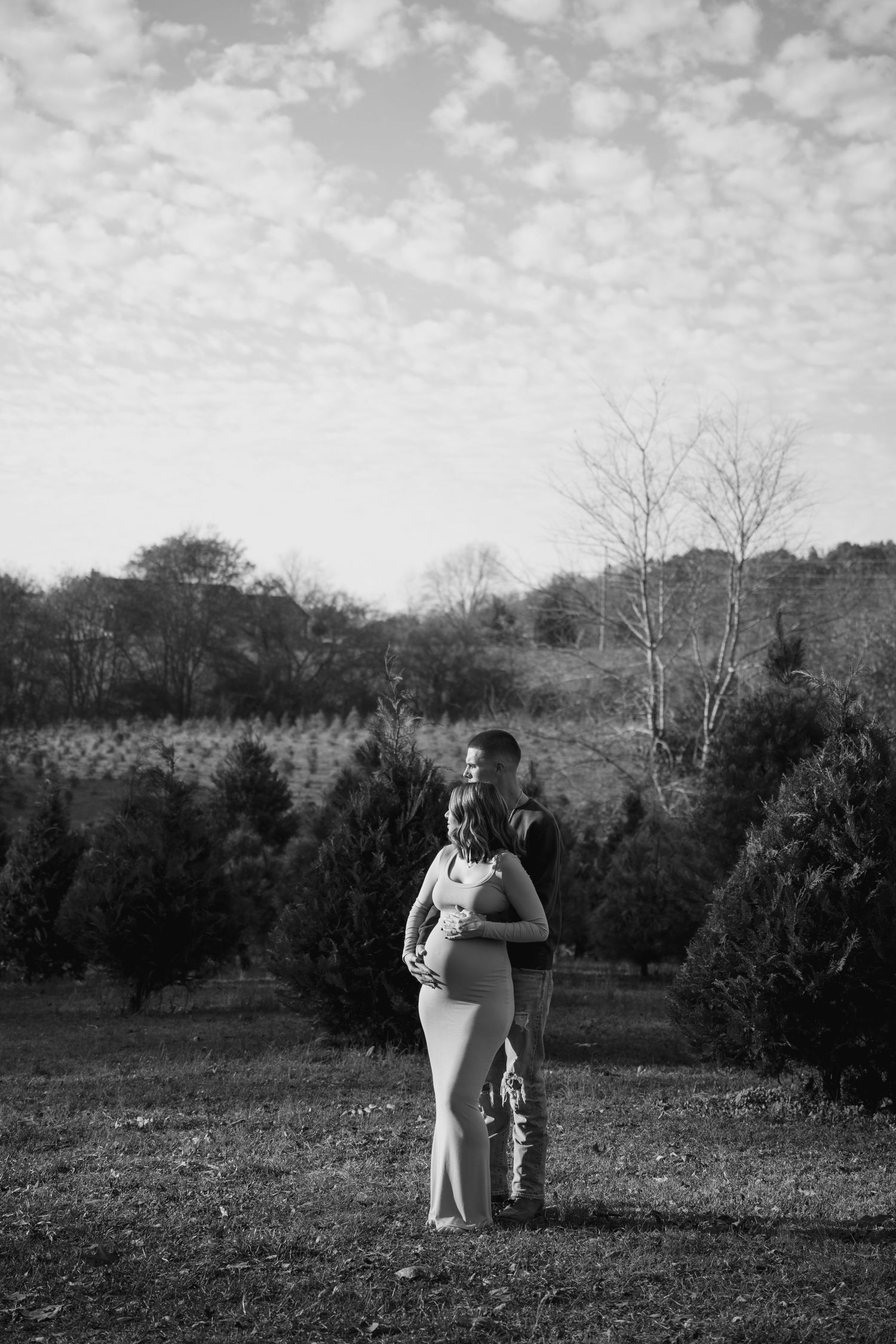 A couple walks together across a grassy field on a cloudy day in black and white photography.