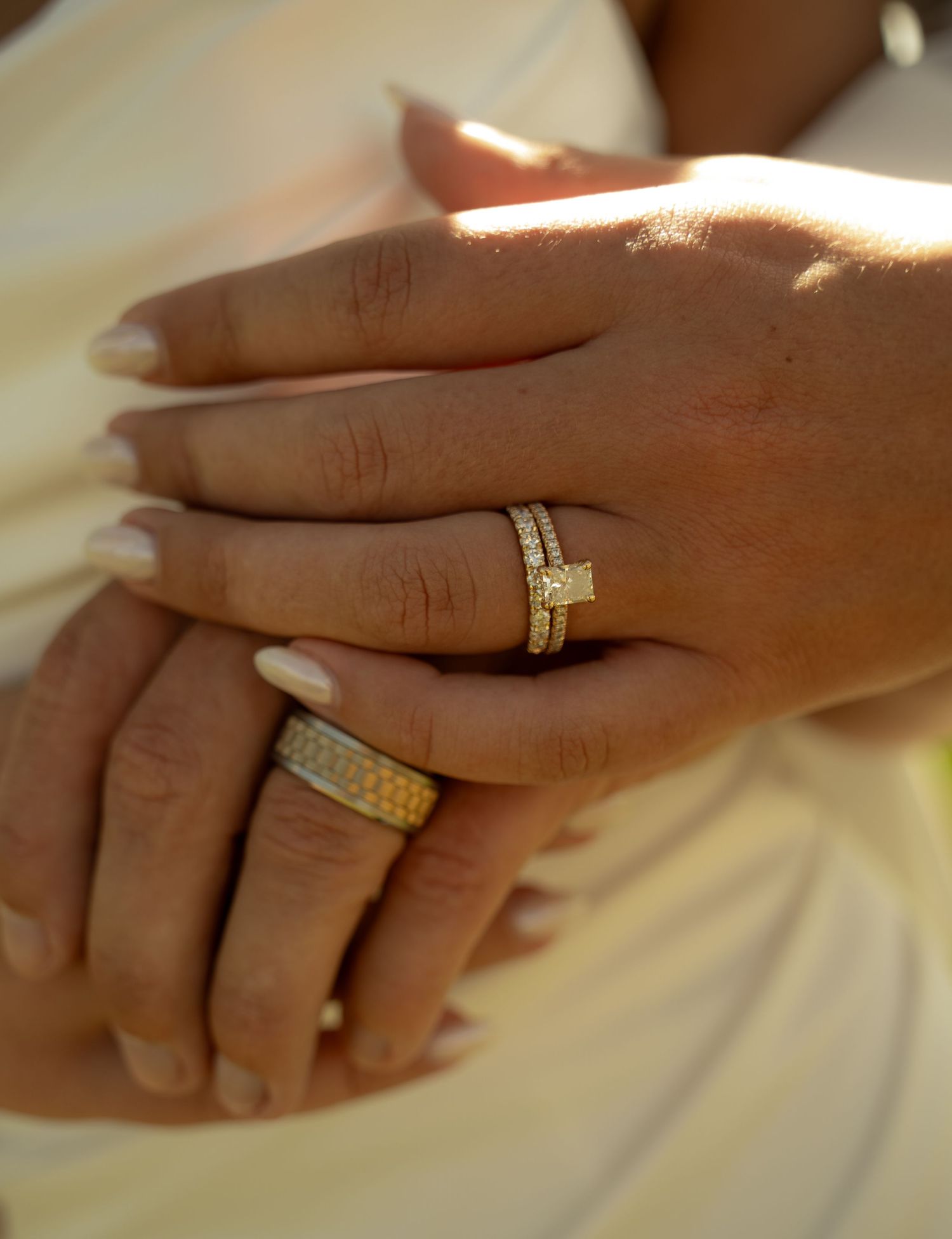 Close-up of two hands adorned with gold diamond wedding and engagement rings on ring fingers.