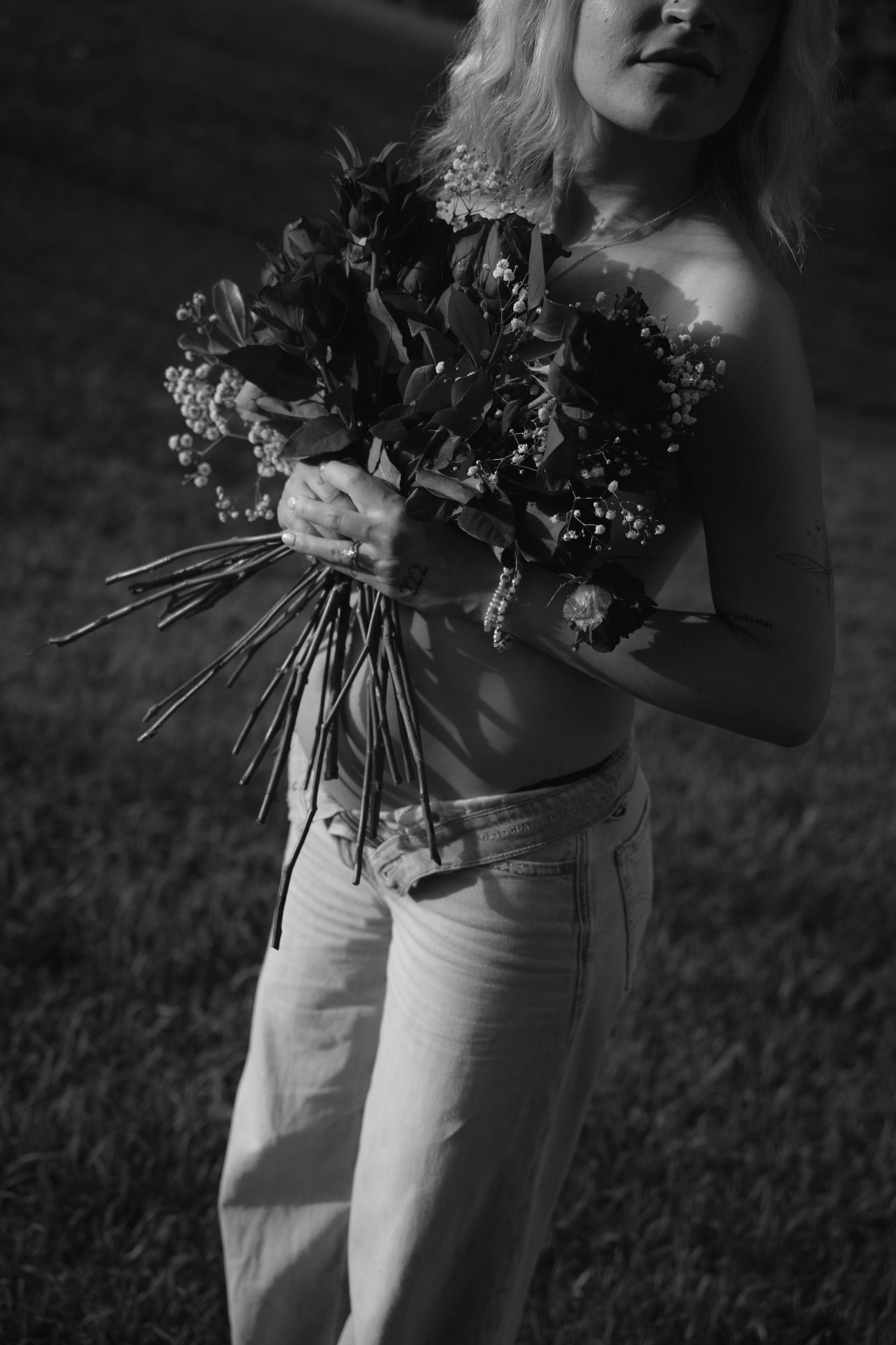 Black and white photo of a woman holding a bouquet of flowers outdoors, wearing jeans and a crop top.