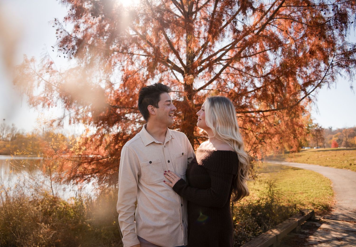 A couple shares a romantic moment in a sunlit autumn park with golden leaves and warm lighting.