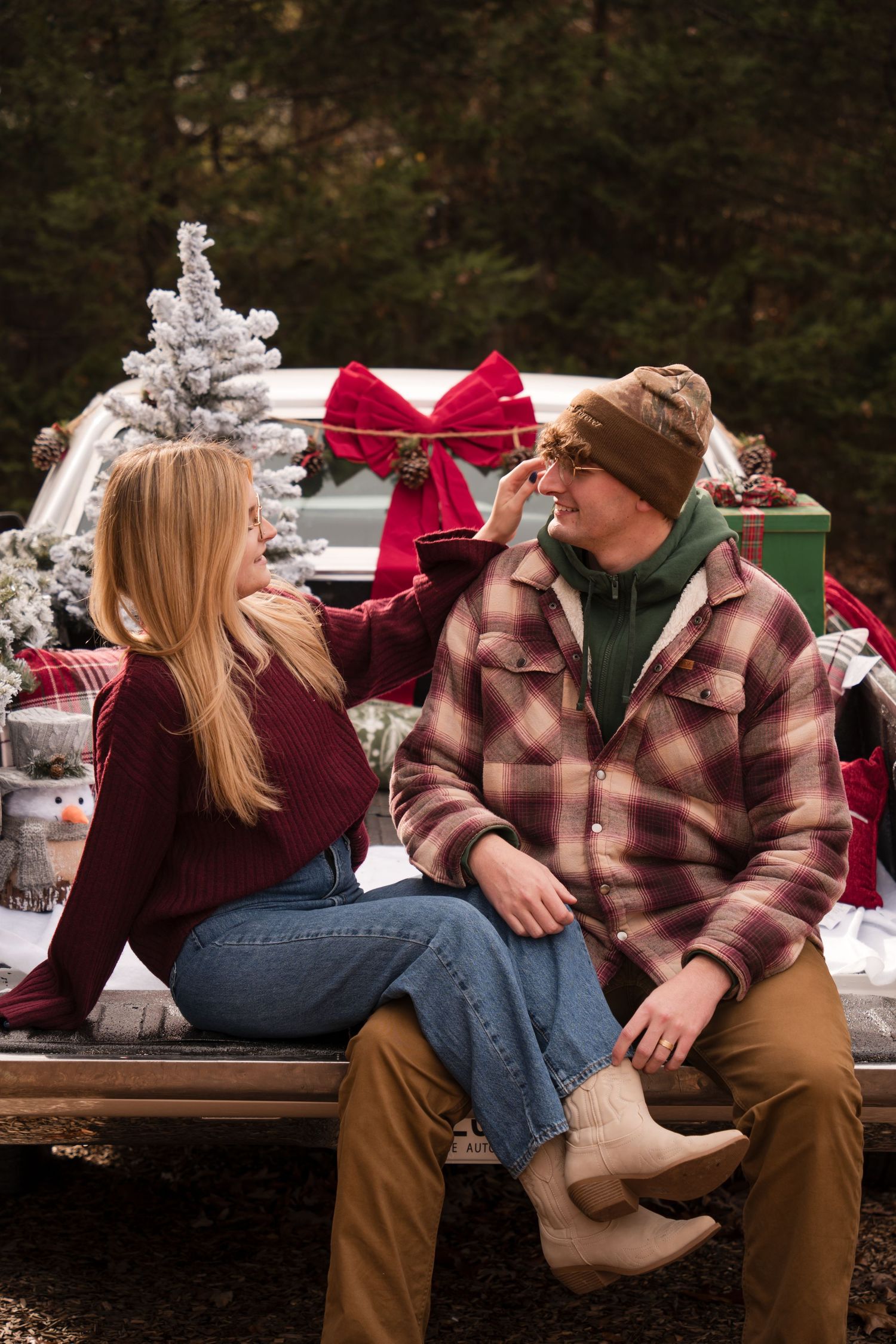 A couple in winter attire sits on a wooden bench in a snowy outdoor setting sharing an intimate moment.