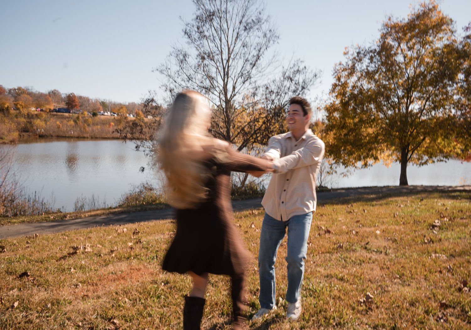A couple dances together on a hillside during autumn with golden leaves and trees in the background.