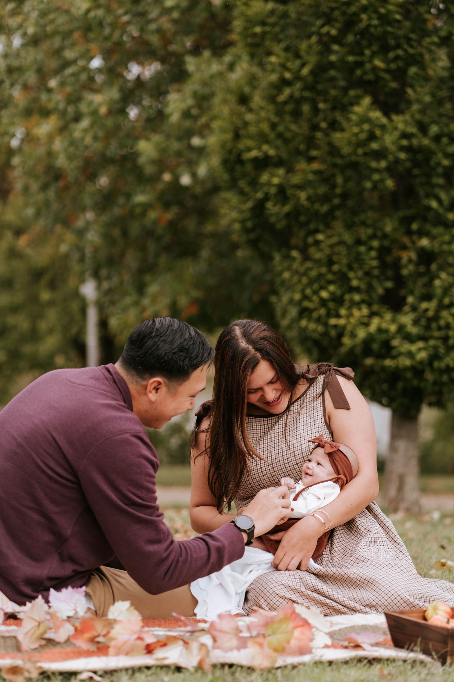 A couple shares tender moments while lying on autumn leaves in a park setting.
