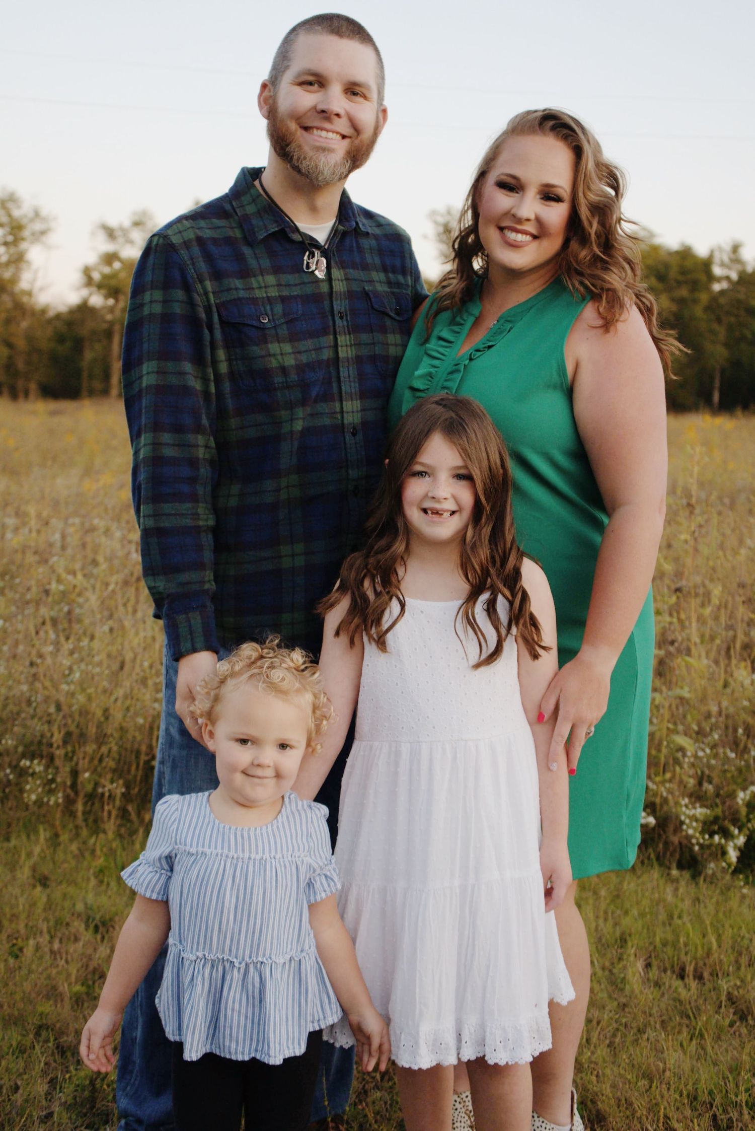 A family poses together in a sunny field wearing coordinated outfits of navy, white and green.