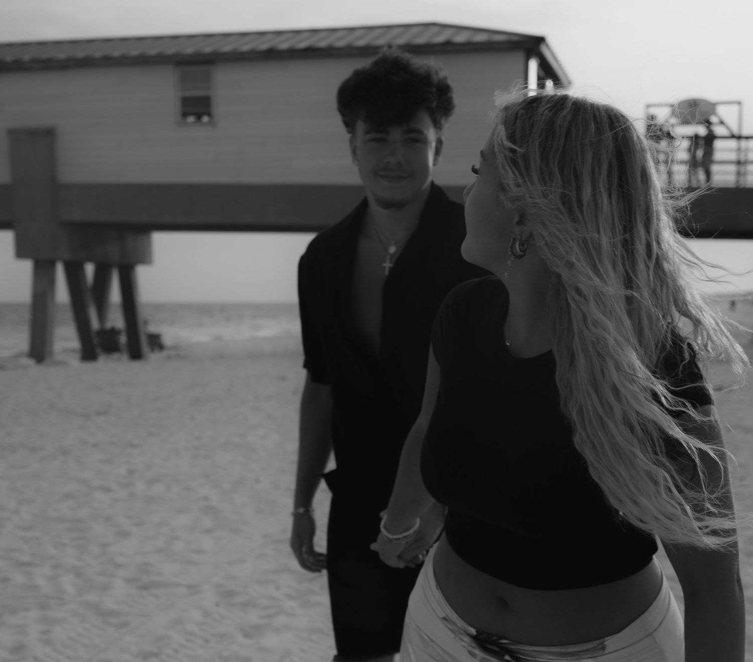 Young couple standing together on beach near pier in black and white photo.