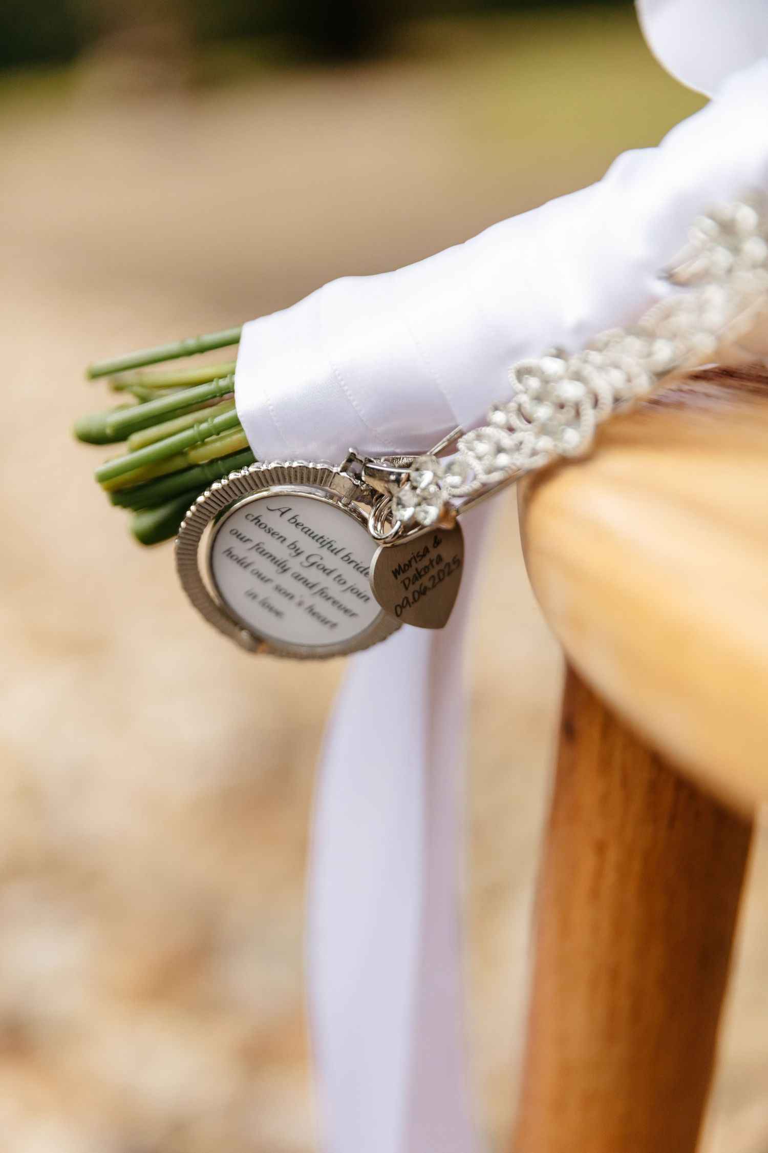 A wedding bouquet wrapped in white ribbon features a delicate silver charm or locket attached to the stem.