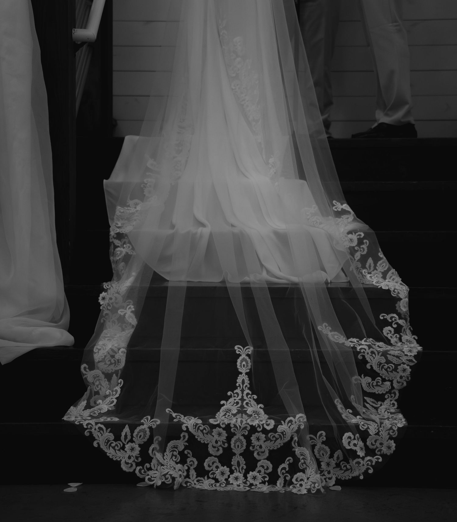 Black and white photo of a bridal veil with intricate lace trim cascading down stairs.