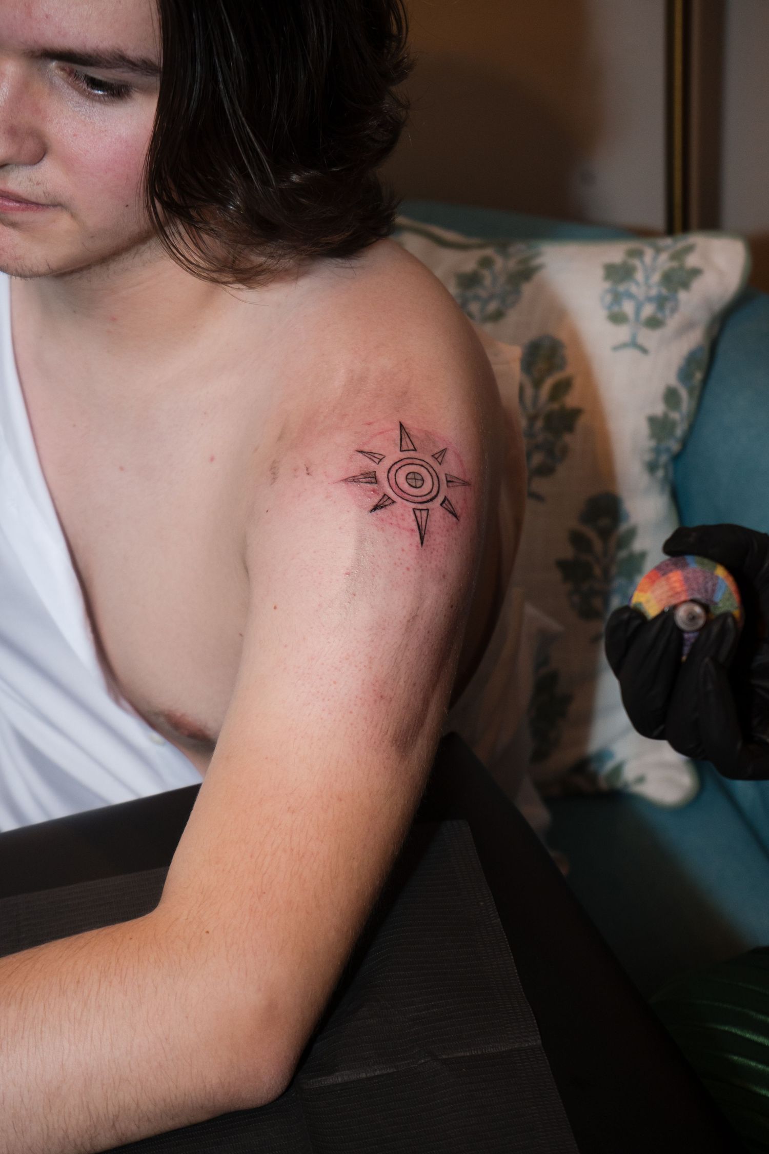 Close-up sequence showing a small sun tattoo design on a person's shoulder in black ink.