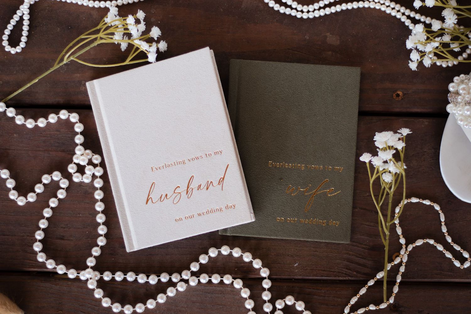 Wedding invitation suite with pearl necklace and elegant calligraphy on dark wooden surface.