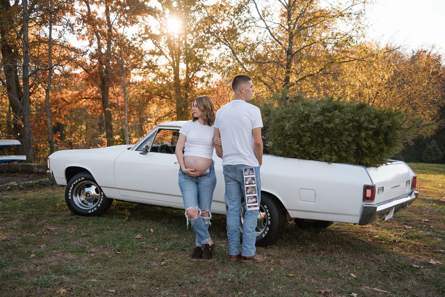 A romantic couple stands beside a classic white car at sunset in an autumn forest setting.