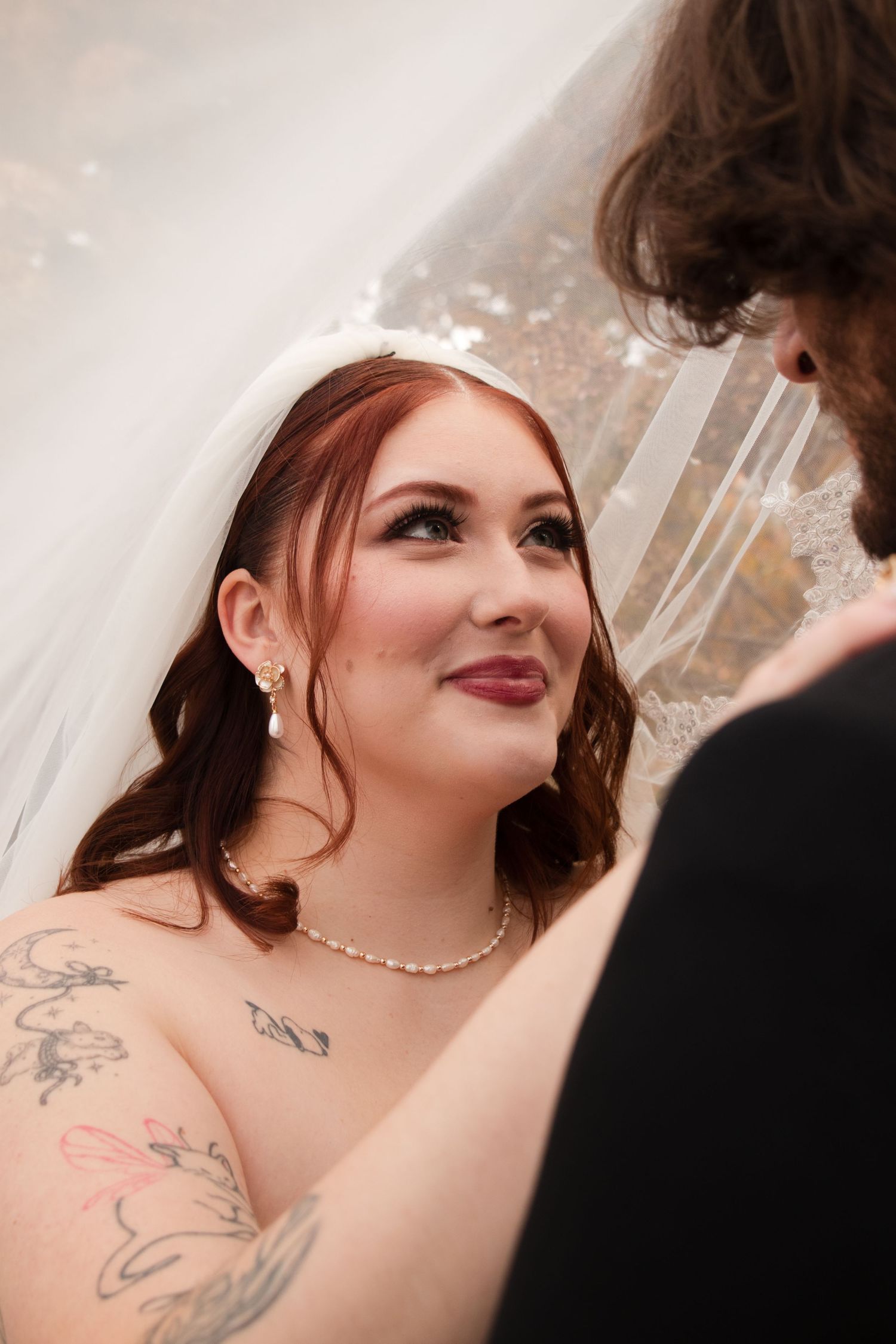 Close up wedding photography showing pearl necklace and floral tattoo details.