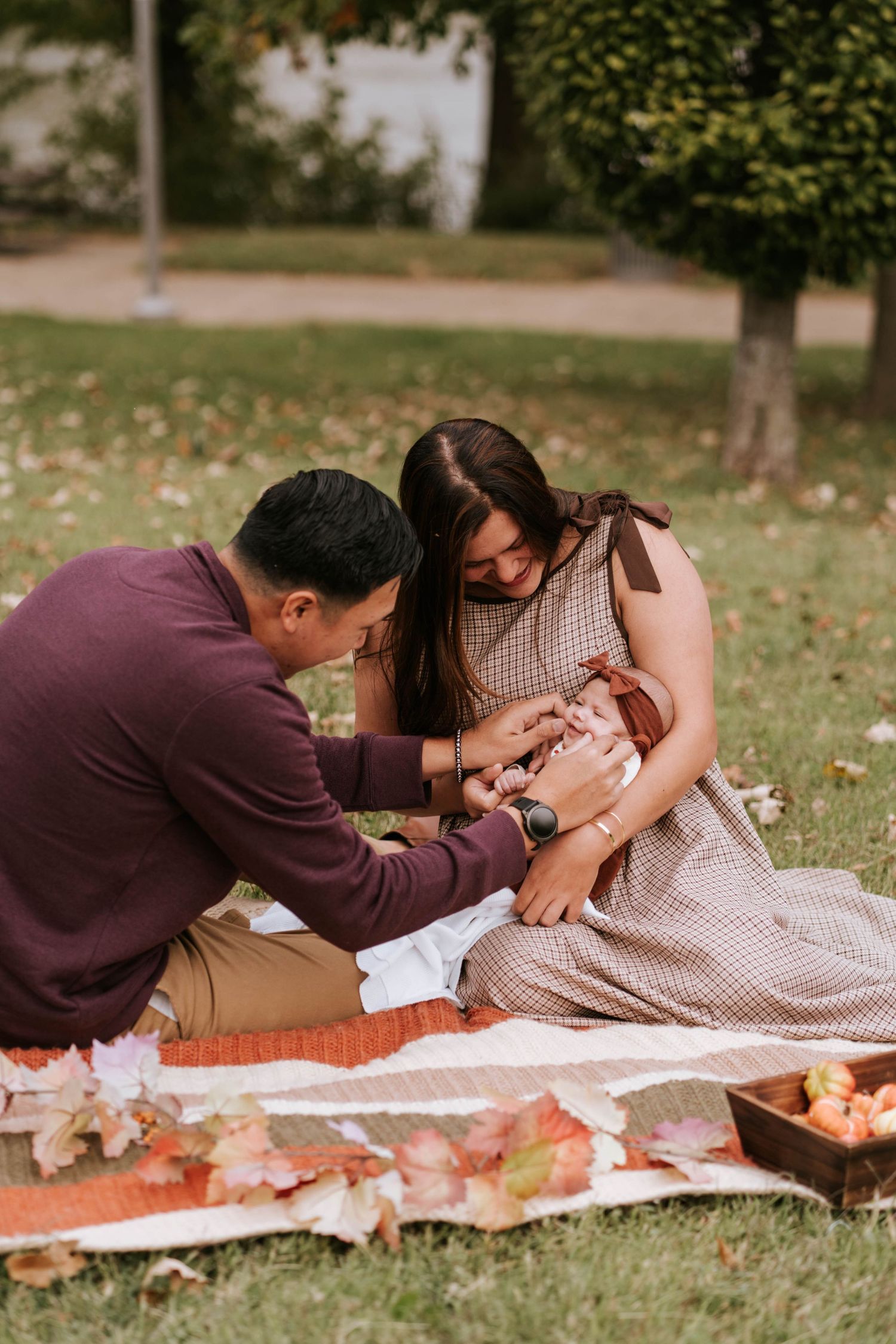 A couple shares an intimate moment while lying on a picnic blanket in a grassy park on an autumn day.