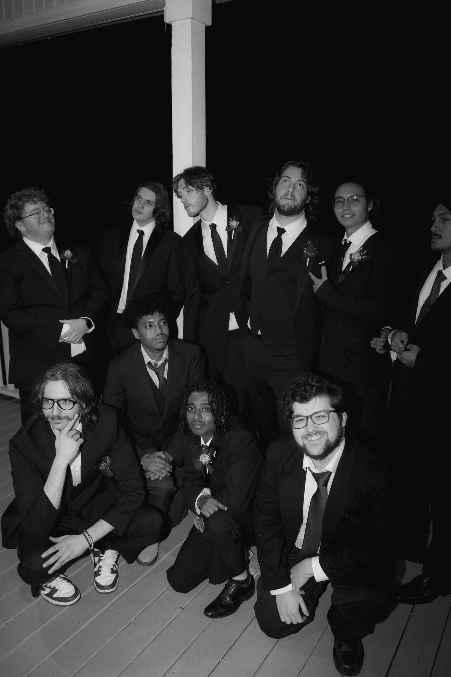 Groomsmen in dark suits pose together on outdoor steps for a formal group photo.