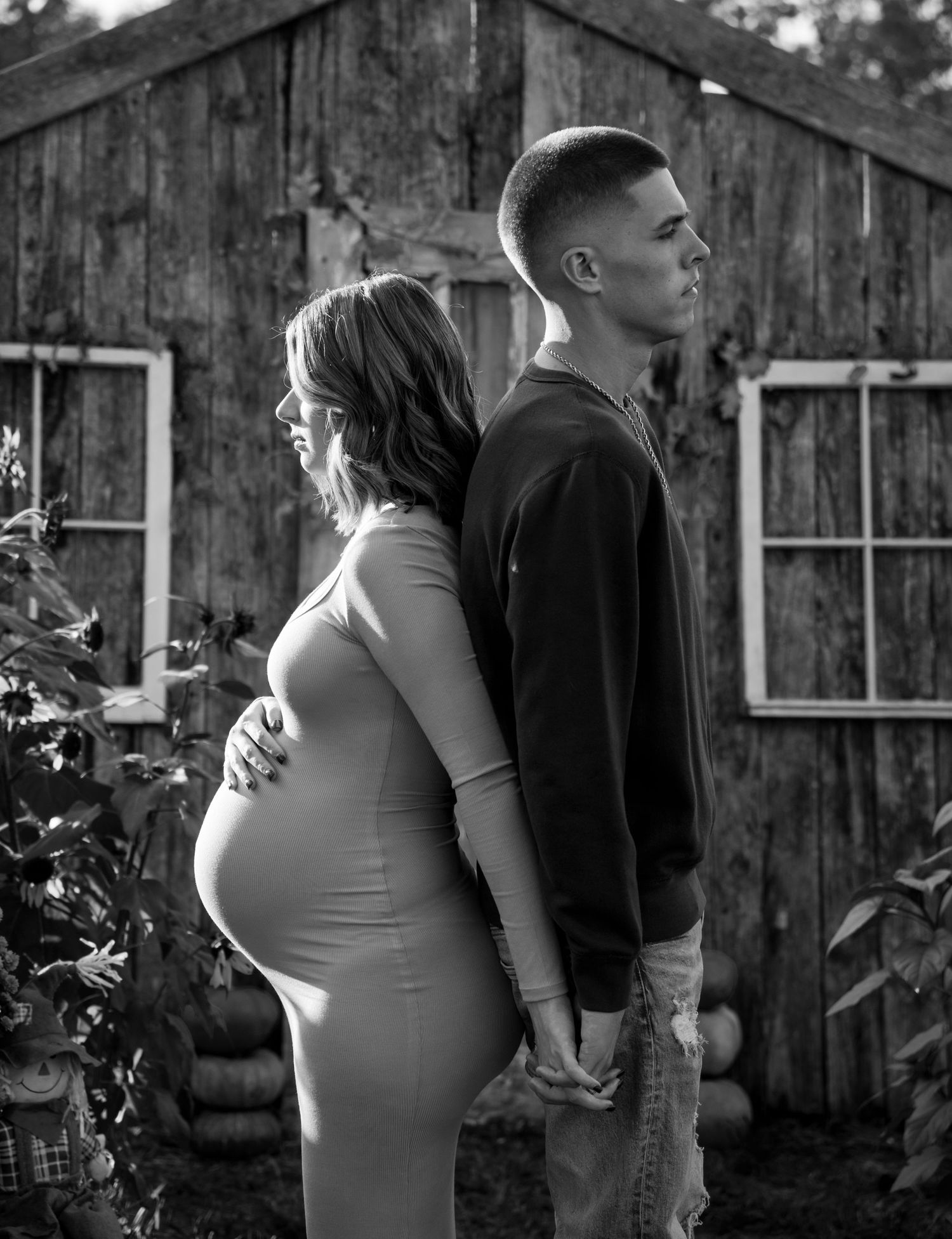 A romantic black and white maternity photo series showing a couple standing together against a rustic wooden wall.