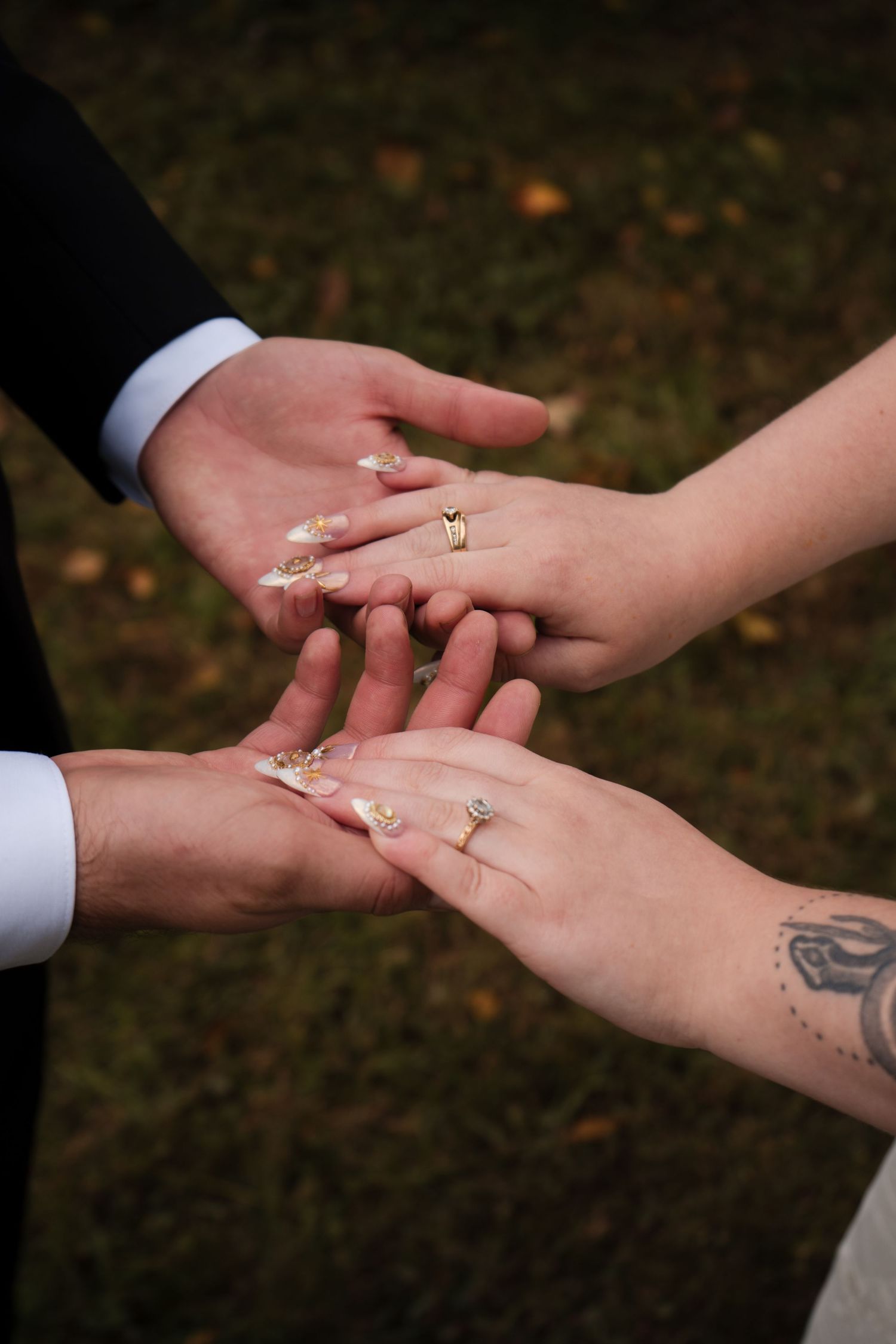 Close-up of hands exchanging rings during wedding ceremony, showing delicate tattoo details.