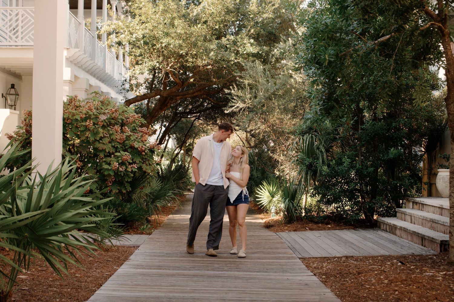 Scenic walkway with tropical plants and white columns leading to historic building.