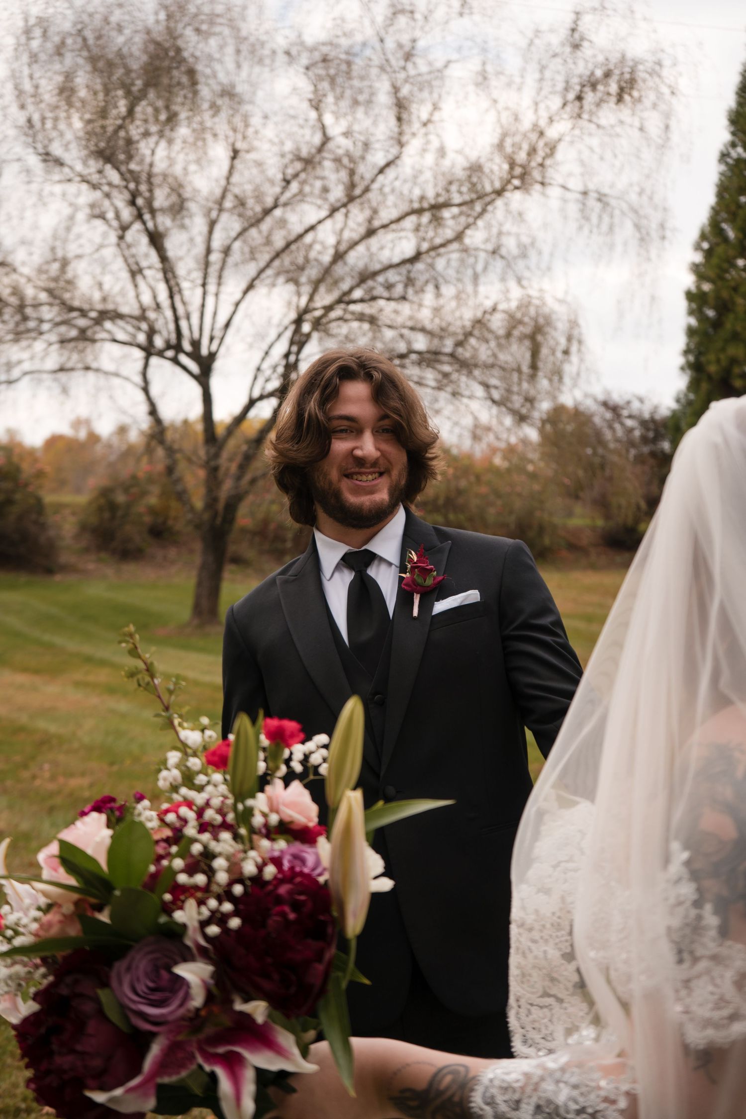 Wedding couple posing with vibrant fall bouquet featuring purple lilies and roses.