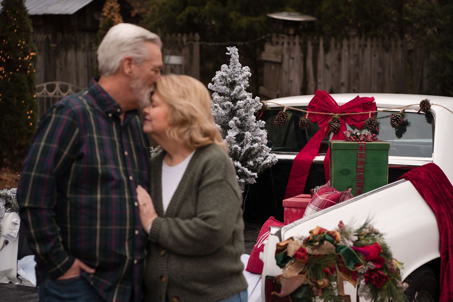 A couple exchanges a romantic kiss outdoors during winter with holiday decorations in the background.