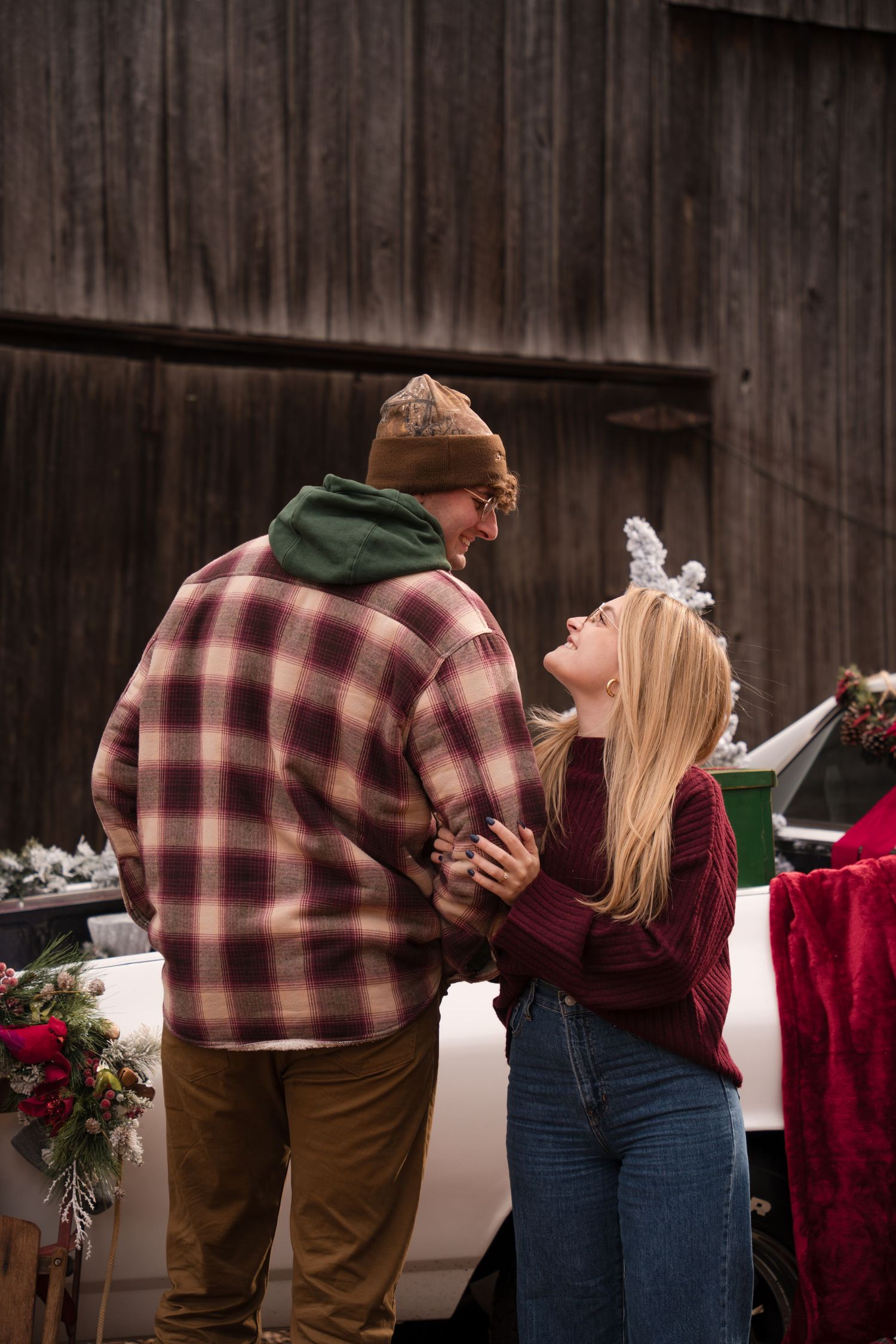 A romantic couple in casual winter attire share intimate moments in a rustic barn setting with holiday decorations.