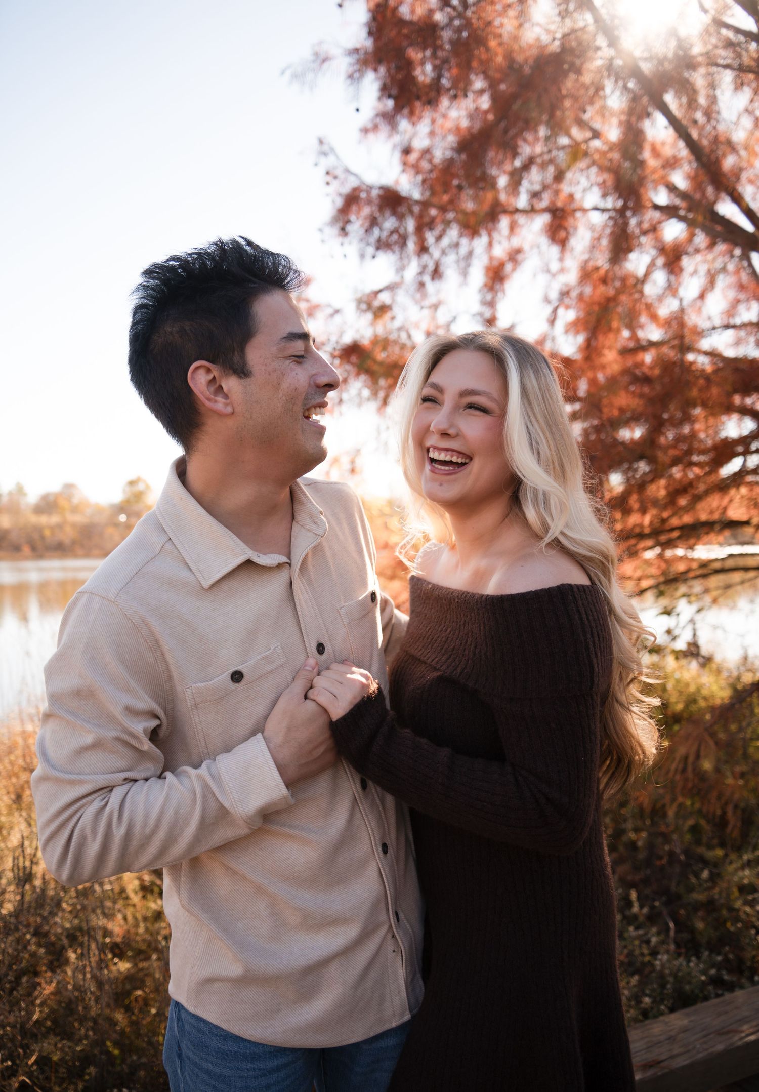 A couple shares joyful laughter together during an autumn sunset photoshoot with warm golden lighting.