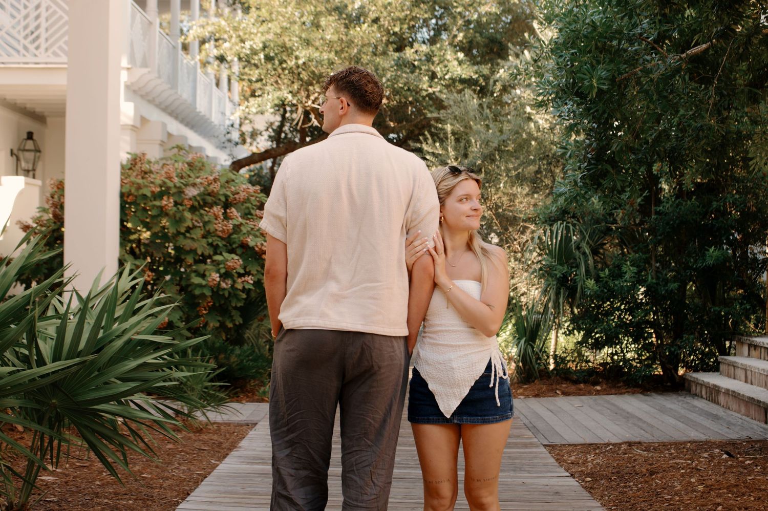 Couple walking along a landscaped pathway beside a white colonial-style building.