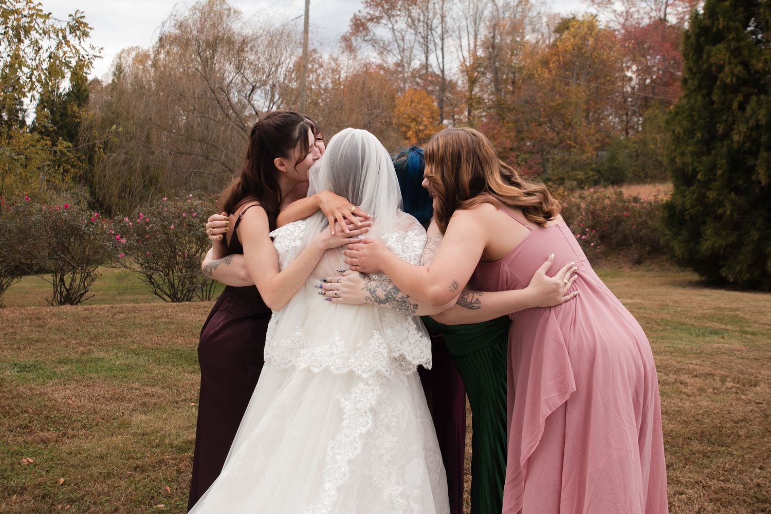 Wedding party in formal attire poses together outdoors during autumn with fall foliage in the background.