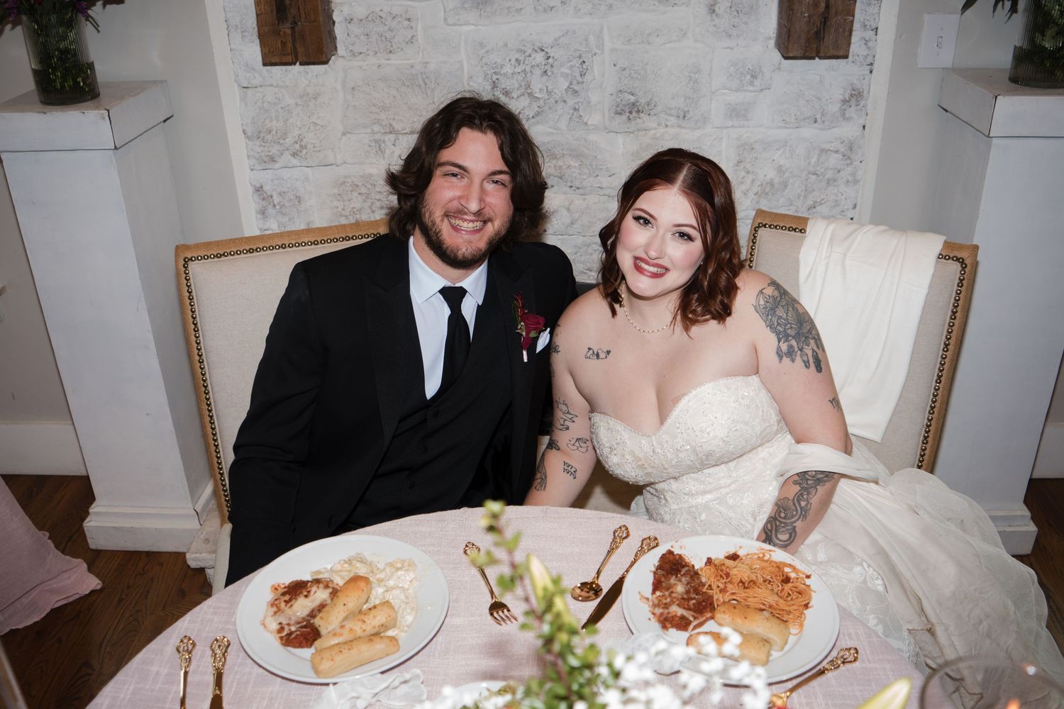 Wedding guests enjoy a reception dinner at rustic tables with exposed stone walls and wooden beams.