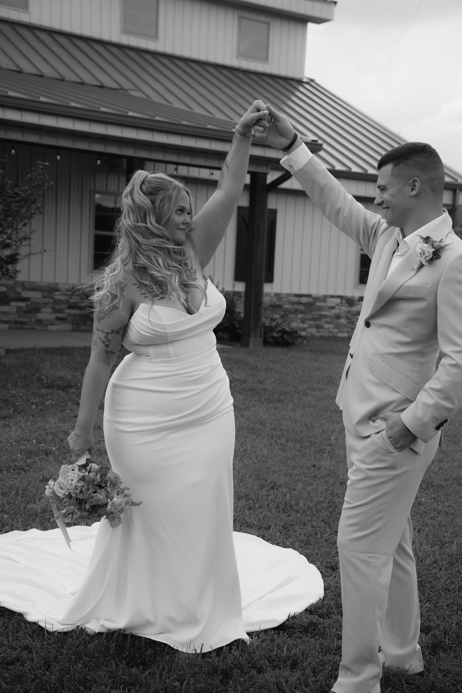 Black and white photo of bride and groom dancing outside rustic barn wedding venue.