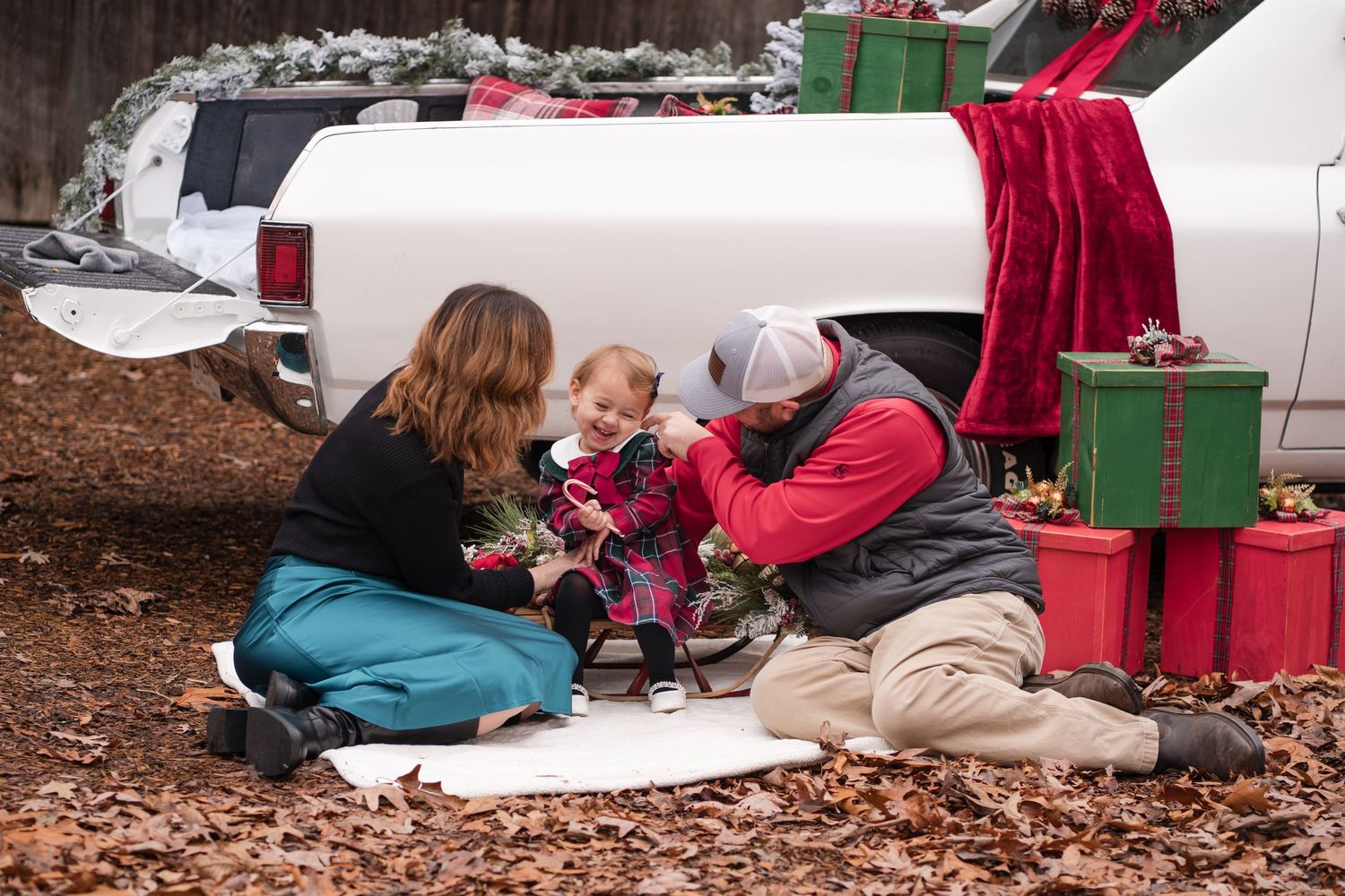 A person in a red jacket examines a small white object while kneeling on the ground near camping equipment.