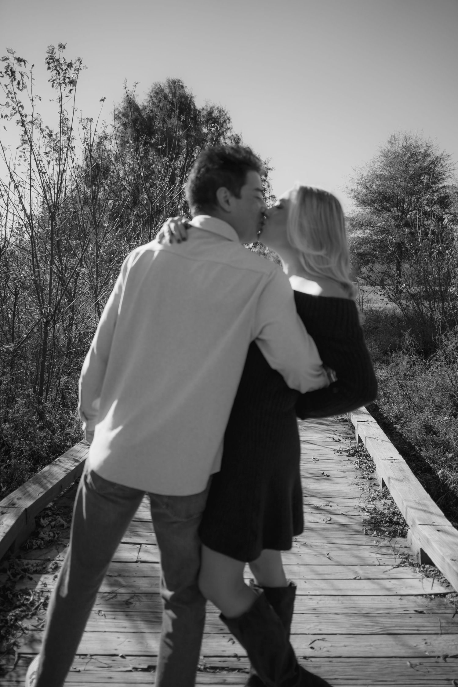 A black and white sequence shows two people walking and leaning together on a wooden boardwalk through nature.