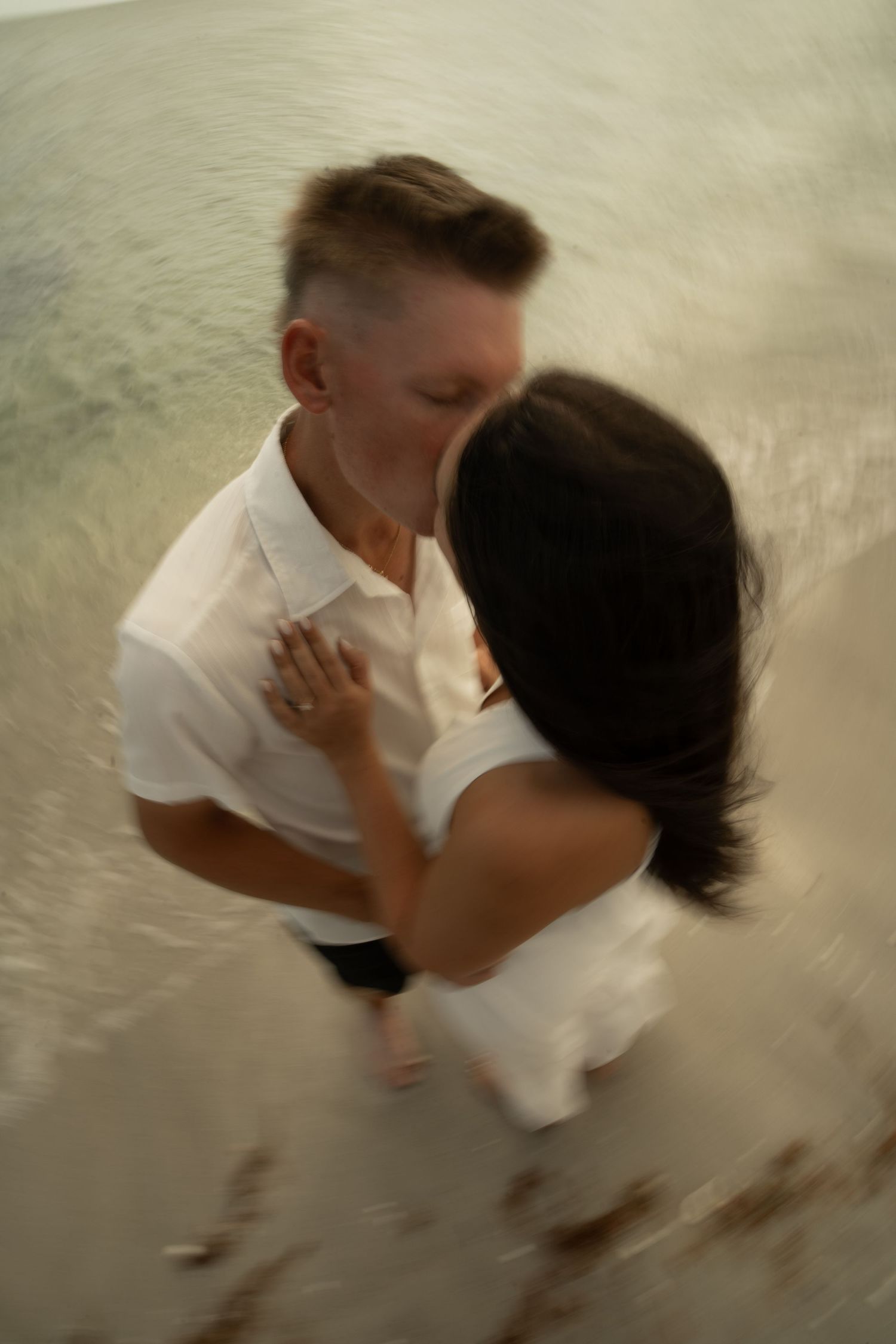 Couple sharing a romantic kiss on the beach, captured with a dreamy motion blur effect near the ocean shoreline.